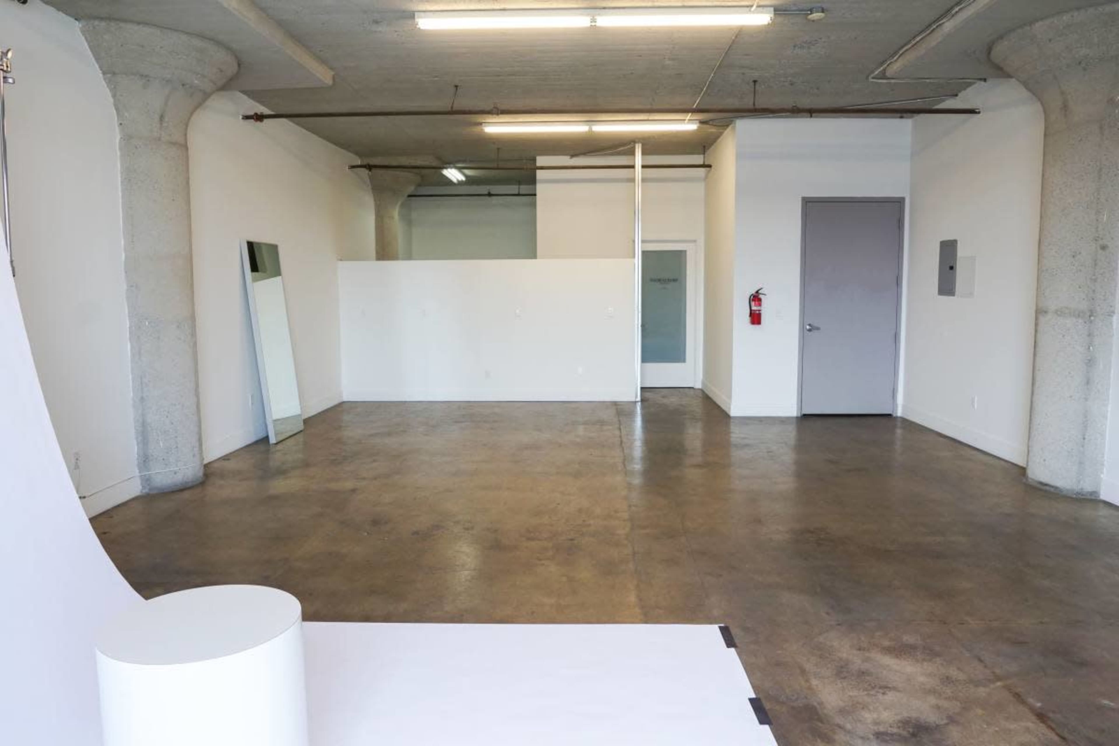 The image shows an empty, spacious room with polished concrete flooring, white walls, and minimal partitioning.