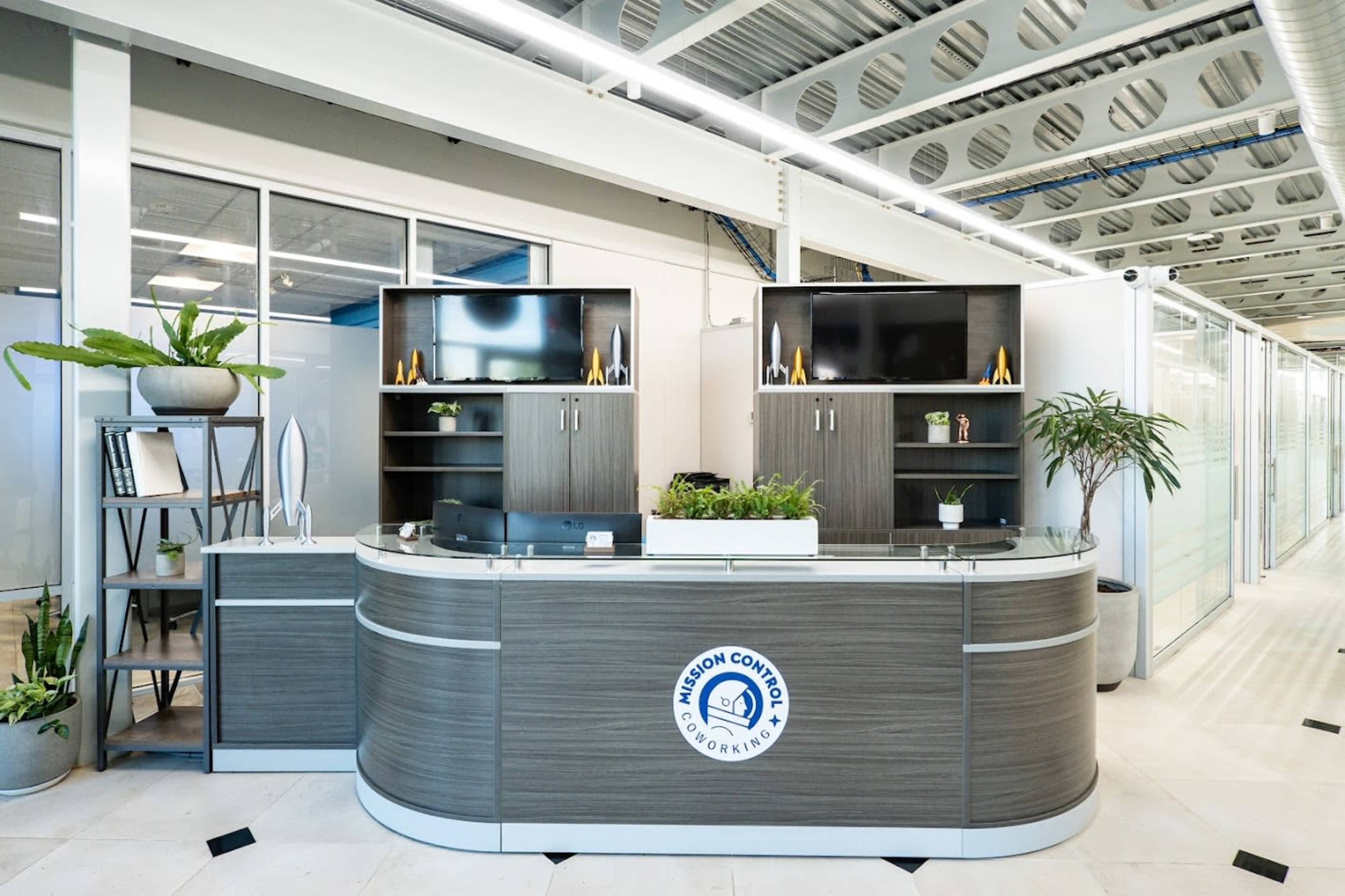 The image depicts a modern office reception area with a curved front desk, shelving units, and potted plants.