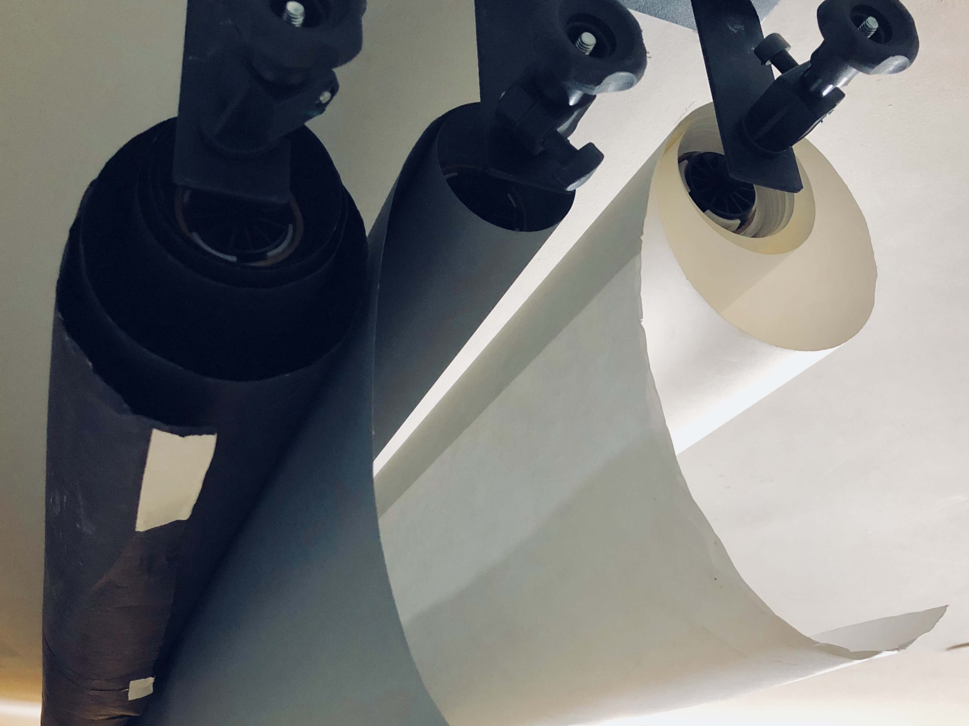 Three large rolls of paper suspended from a ceiling-mounted holder.