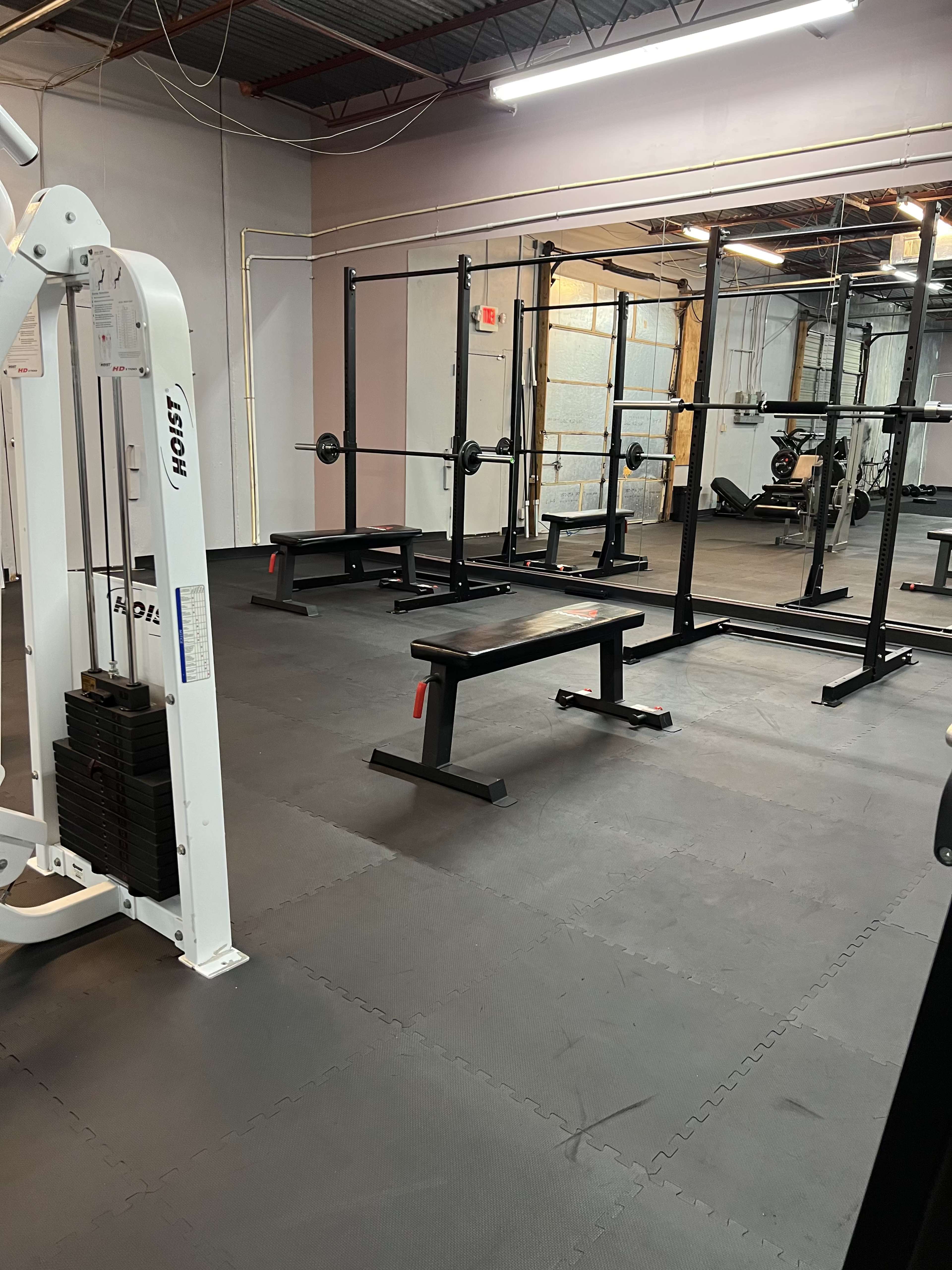 An empty gym with various pieces of exercise equipment, including a weight bench and a squat rack.