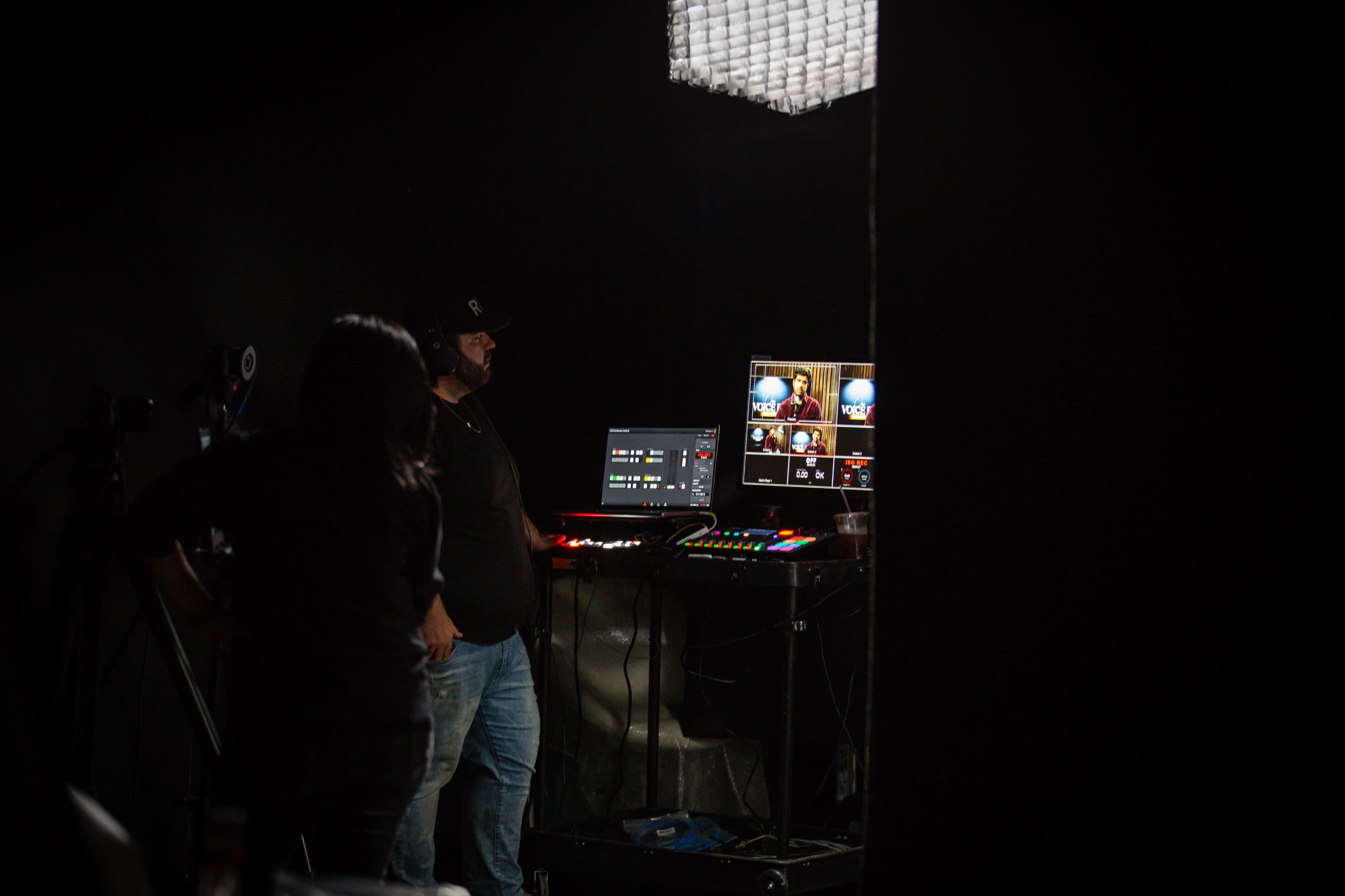 A person operates a video production setup in a dimly lit room.