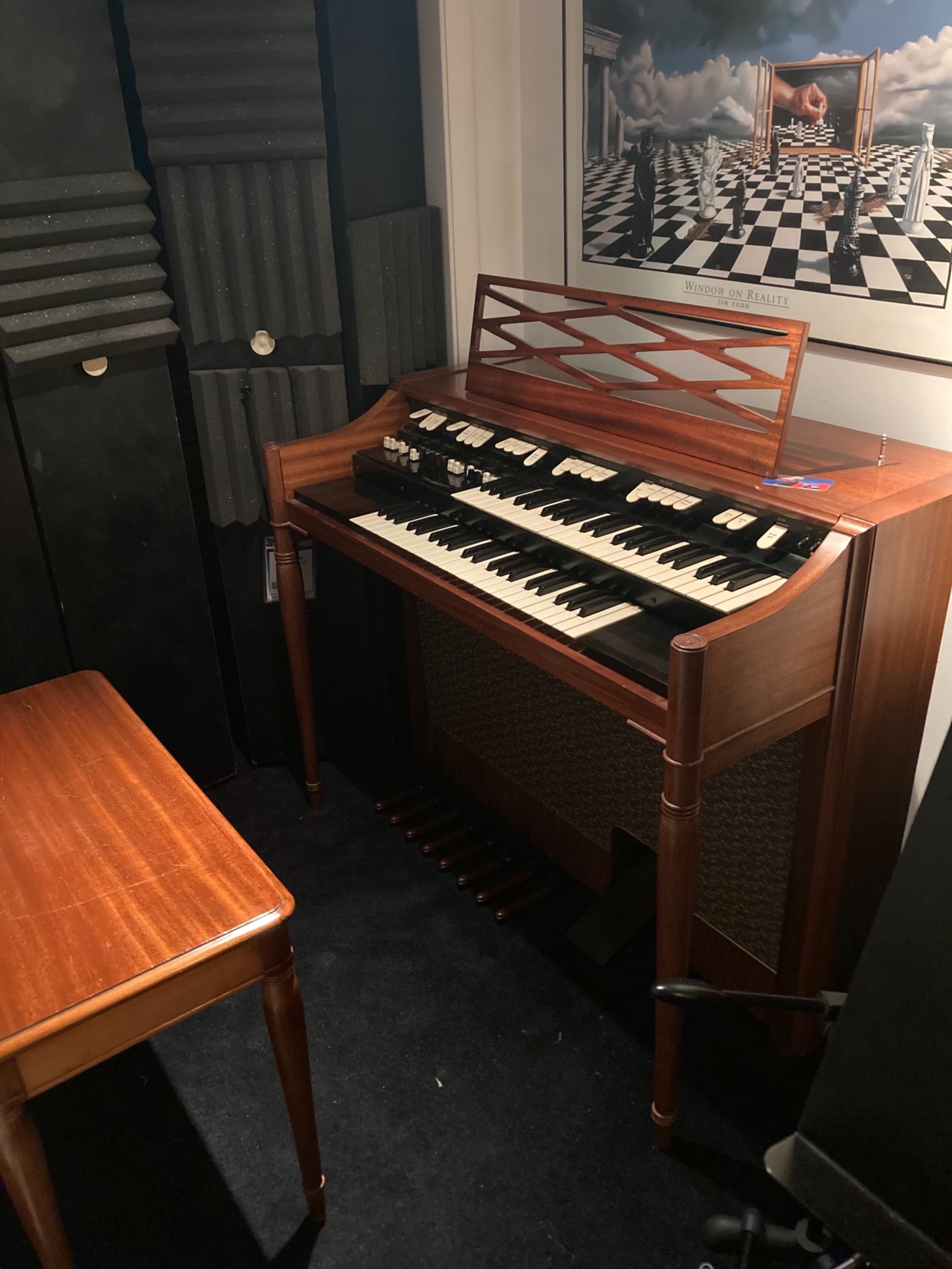 A wooden organ next to a small table in a room with soundproofing panels.
