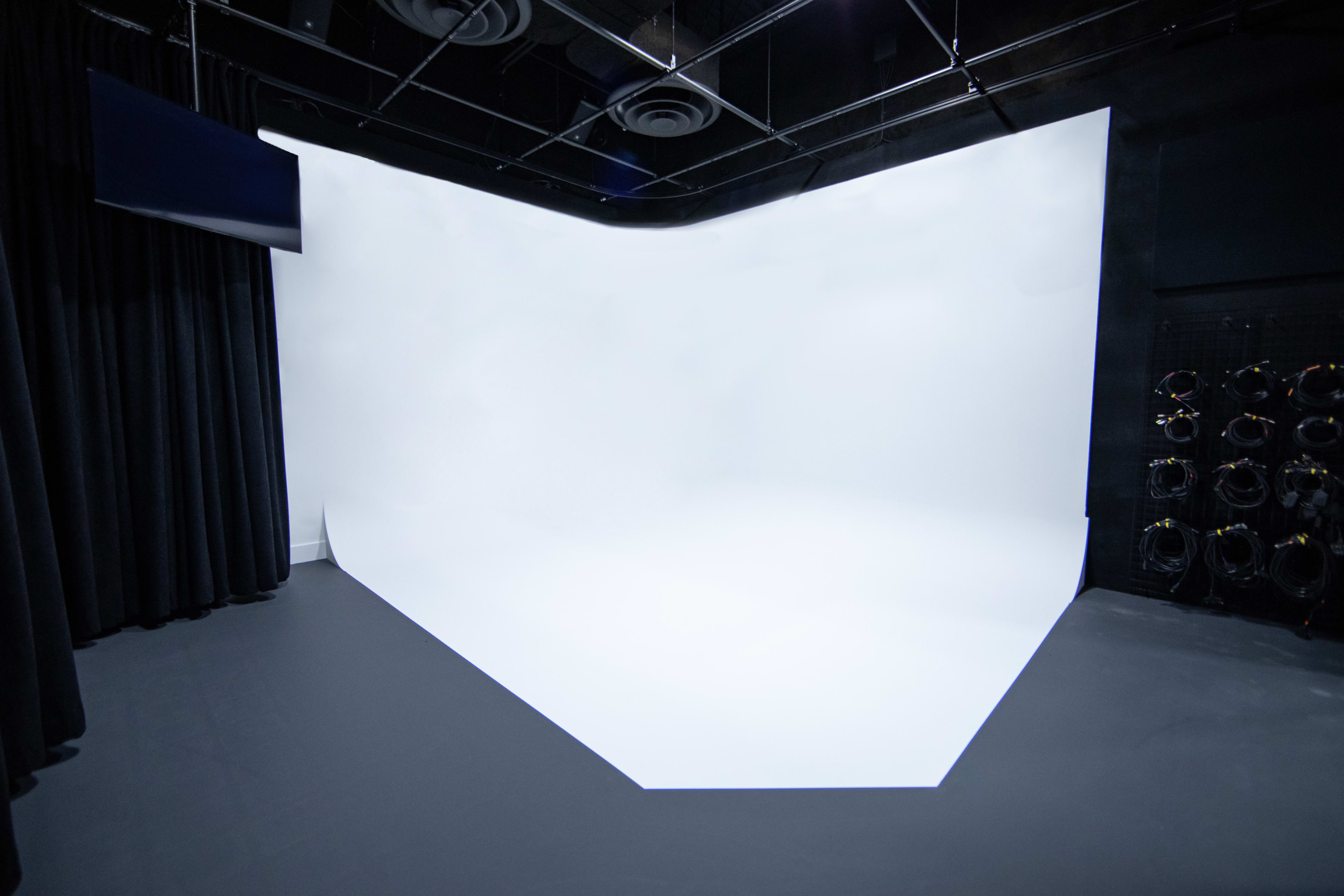 An empty photography studio with a seamless white backdrop and dark curtains on one side.