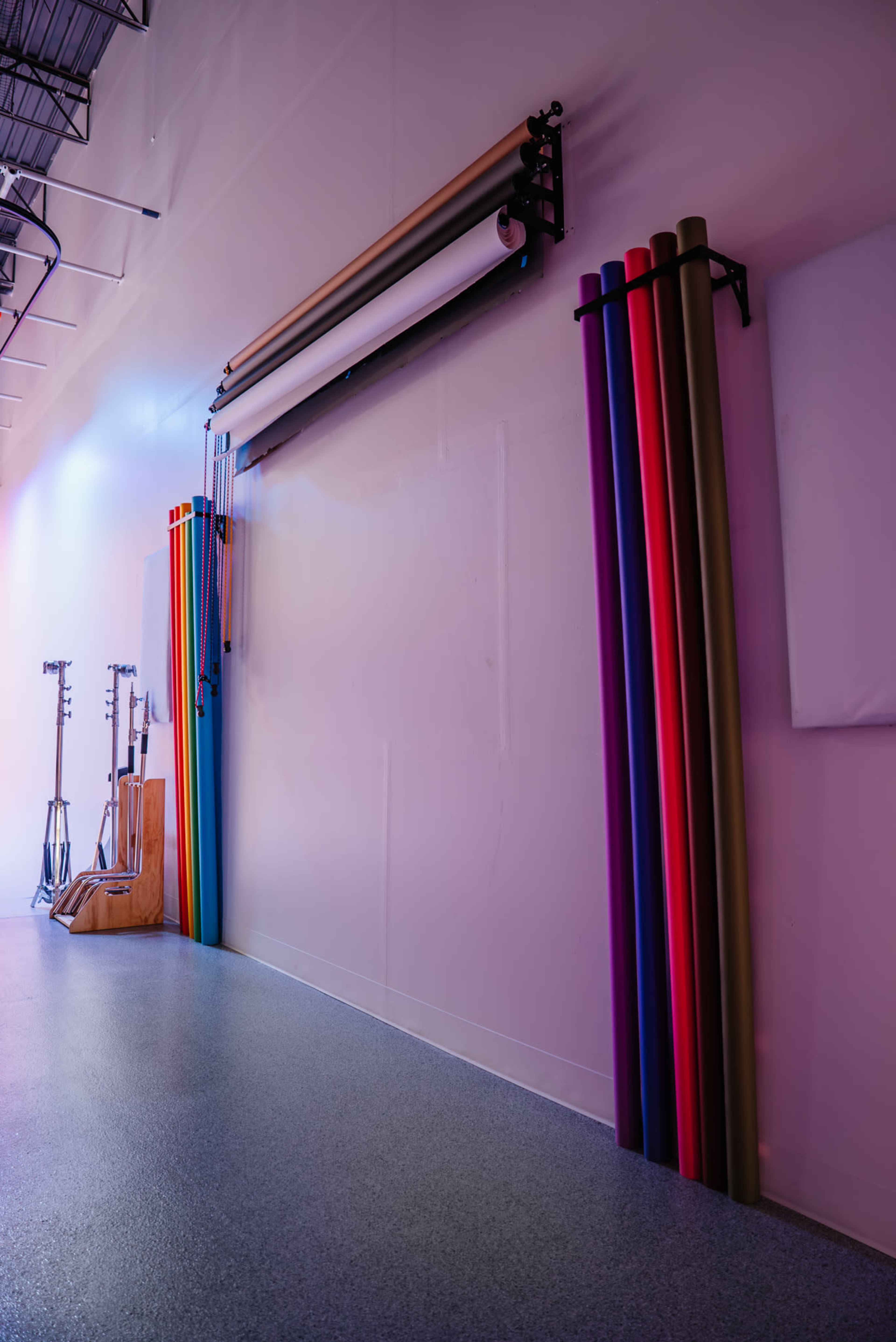 The image shows a studio interior with a wall displaying various colored backdrop rolls and studio lighting equipment arranged on the floor.