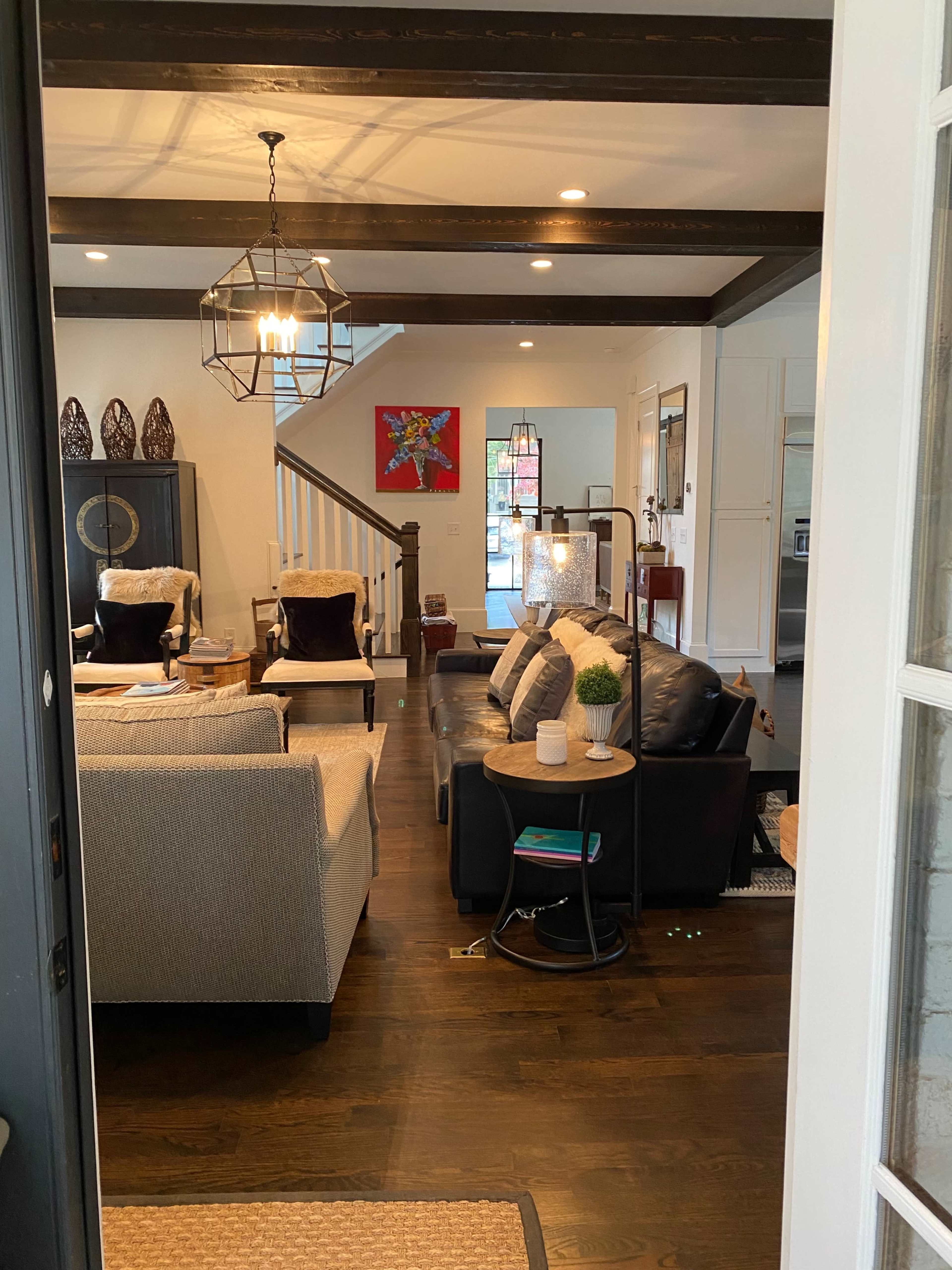 The image shows a well-lit living room with a mix of seating areas, decorative elements, and a staircase leading to the upper level.