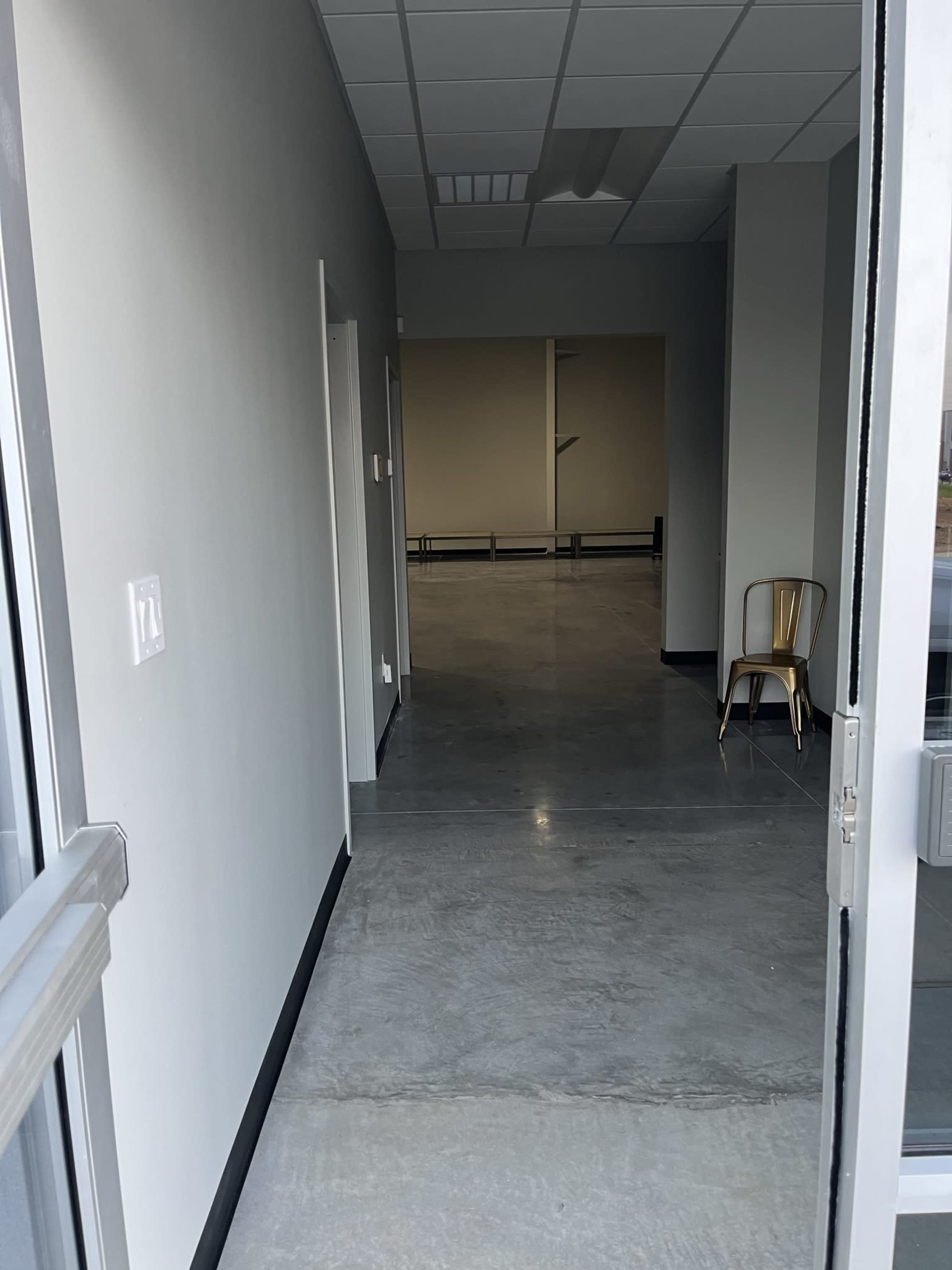A long corridor leading to an empty room, with a metal chair positioned against the wall.