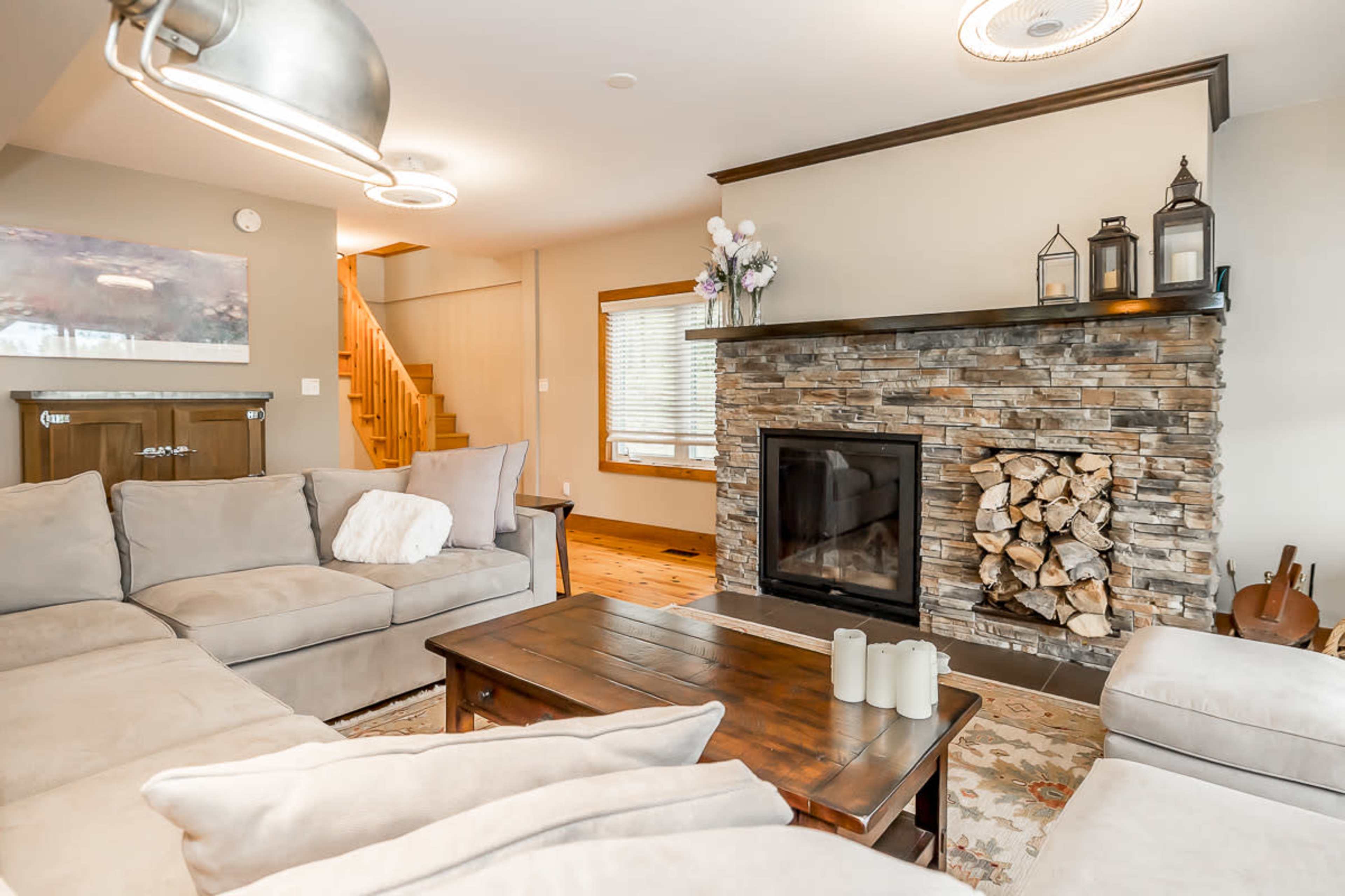 The living room features a stone fireplace with stacked logs, surrounded by a sectional sofa and a wooden coffee table.