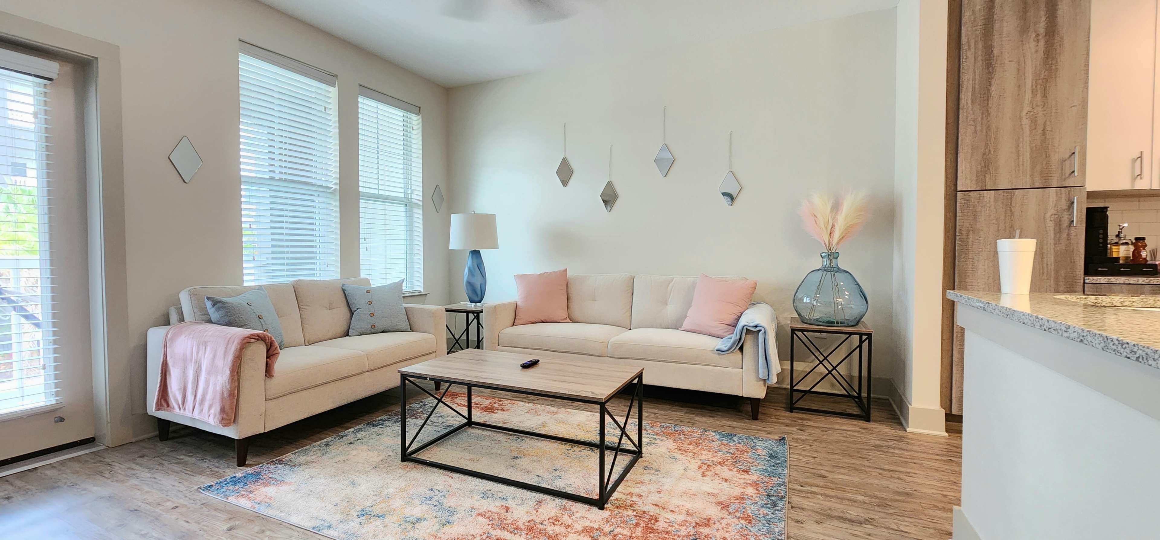 A modern living room featuring a beige sofa and loveseat, a glass coffee table, and decorative elements like a floor lamp and a large vase.