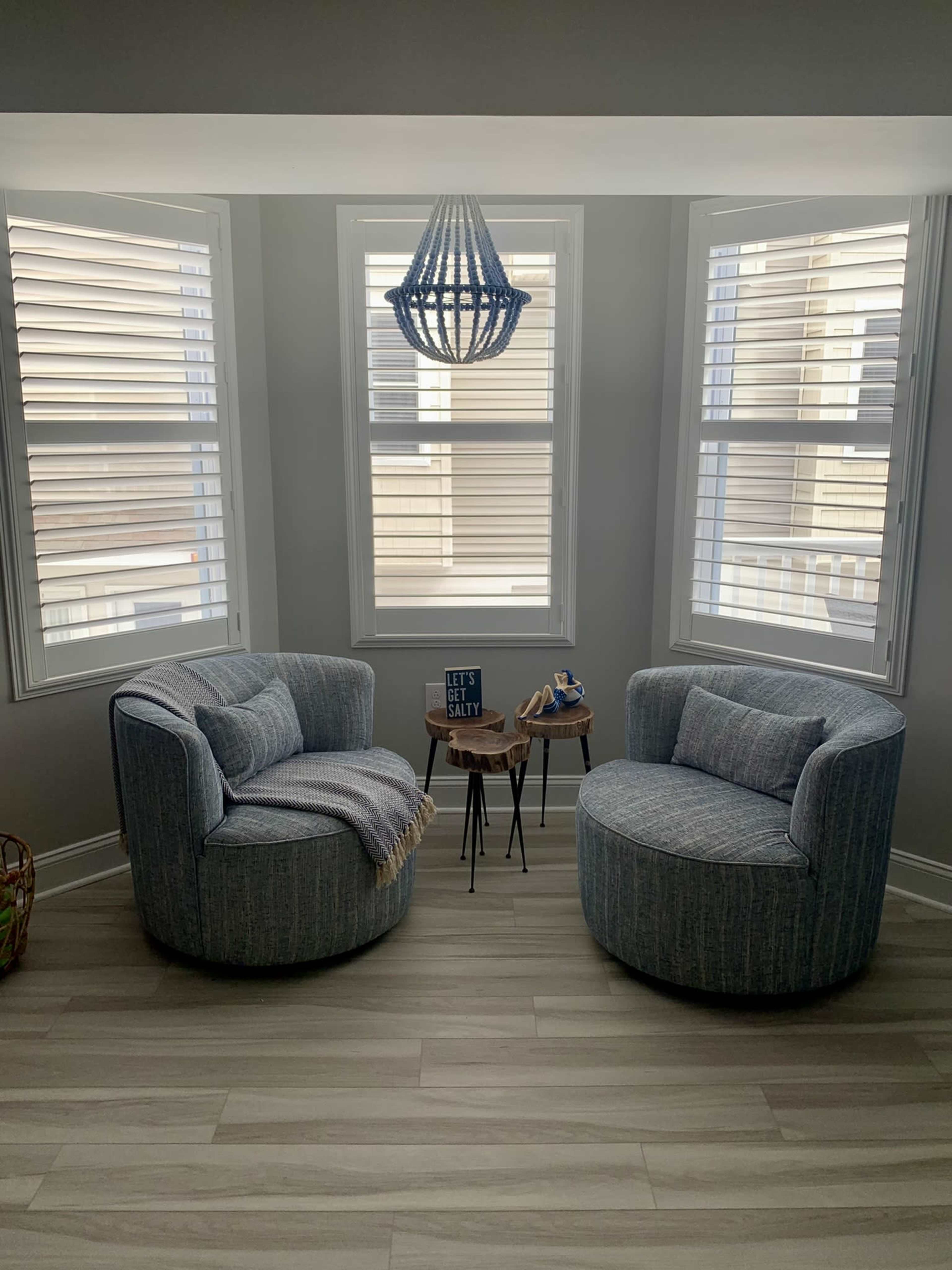 Two upholstered chairs are positioned beside a small table in a well-lit corner, featuring a patterned throw and a modern chandelier above.