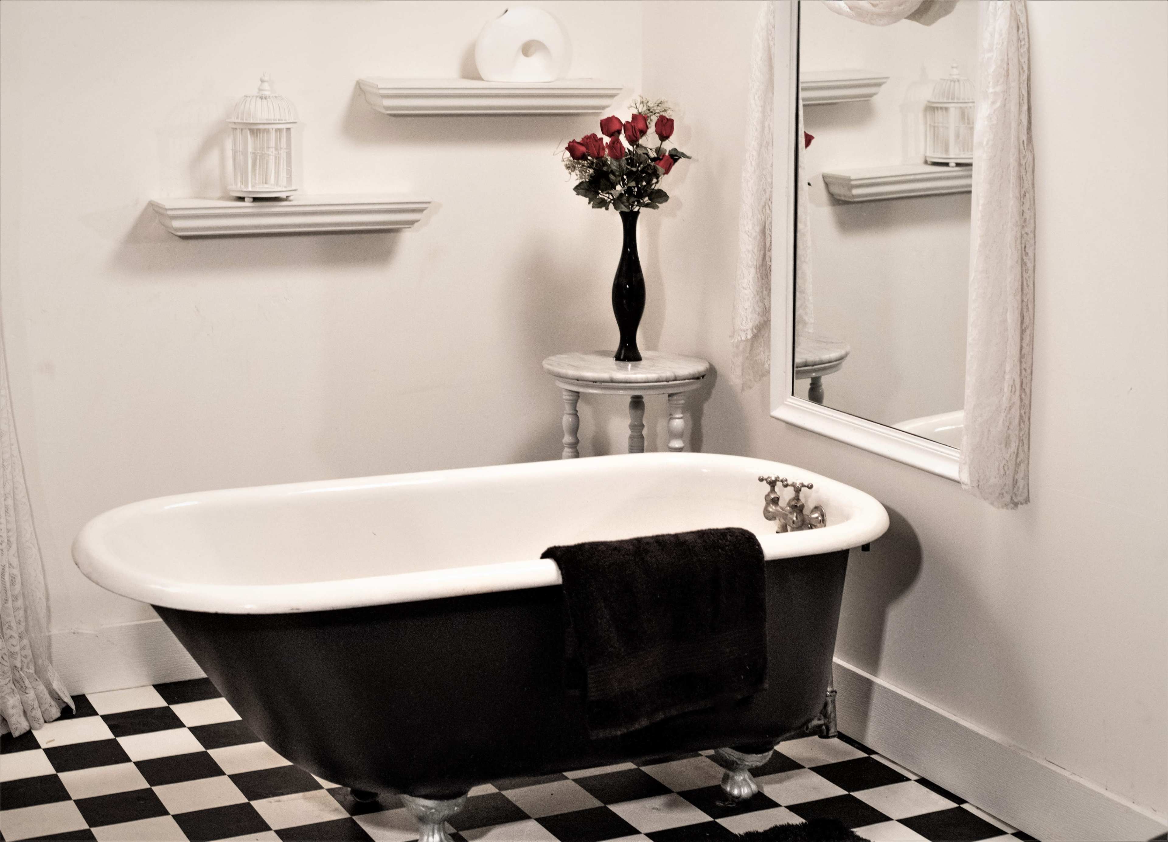 A black and white checkered bathroom features a vintage clawfoot bathtub, a vase of roses on a small table, and a wall mirror.