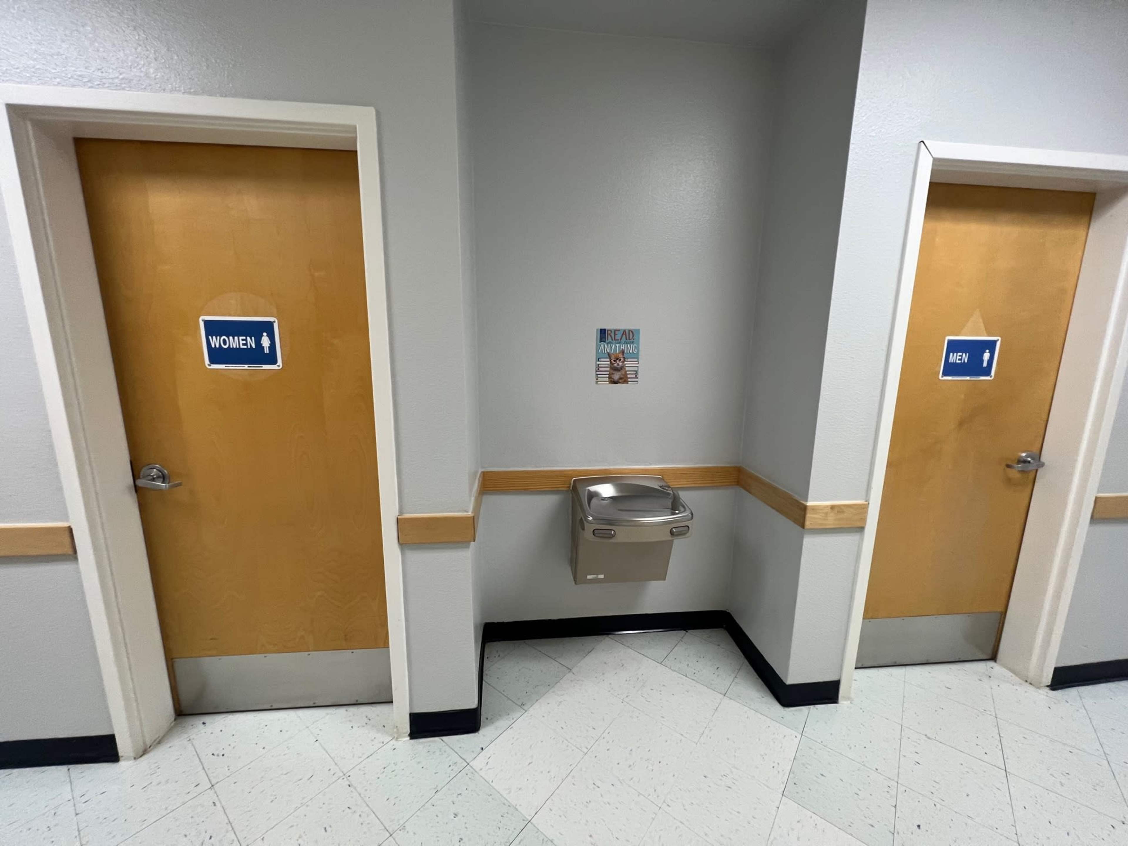 Two restroom doors labeled "WOMEN" and "MEN," with a water fountain located in between them.