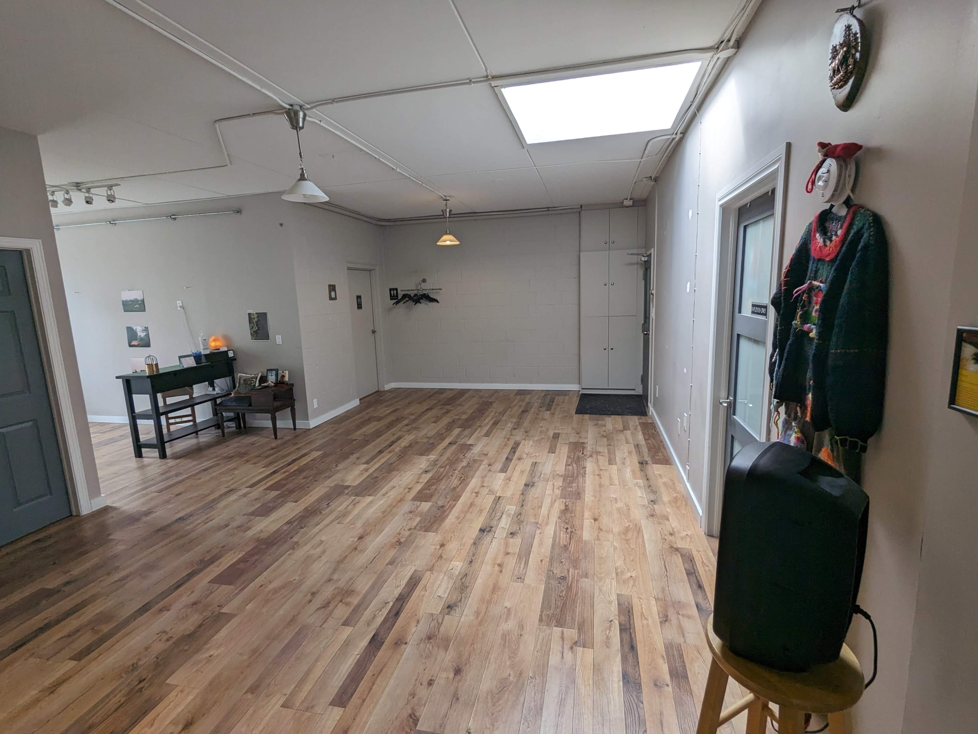 A spacious, empty interior room with wooden flooring, a skylight, and a few pieces of furniture against the walls.