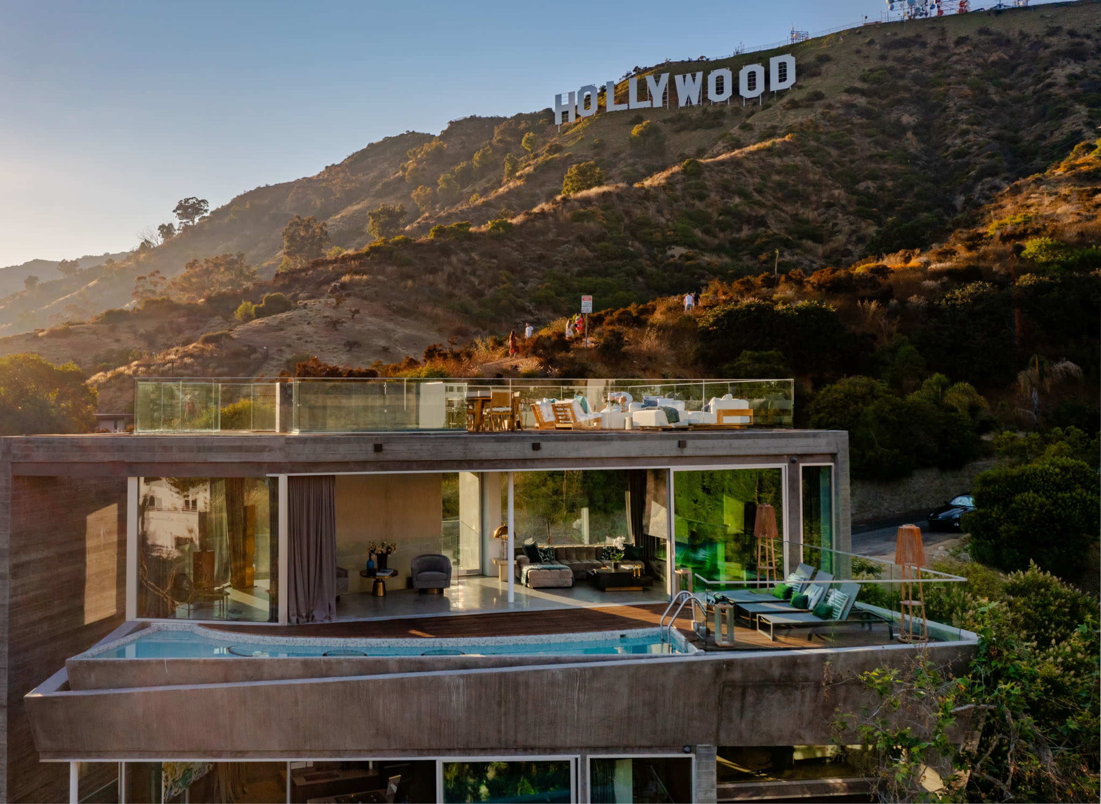 A modern house with a pool is situated on a hillside, overlooking the Hollywood sign in the background.