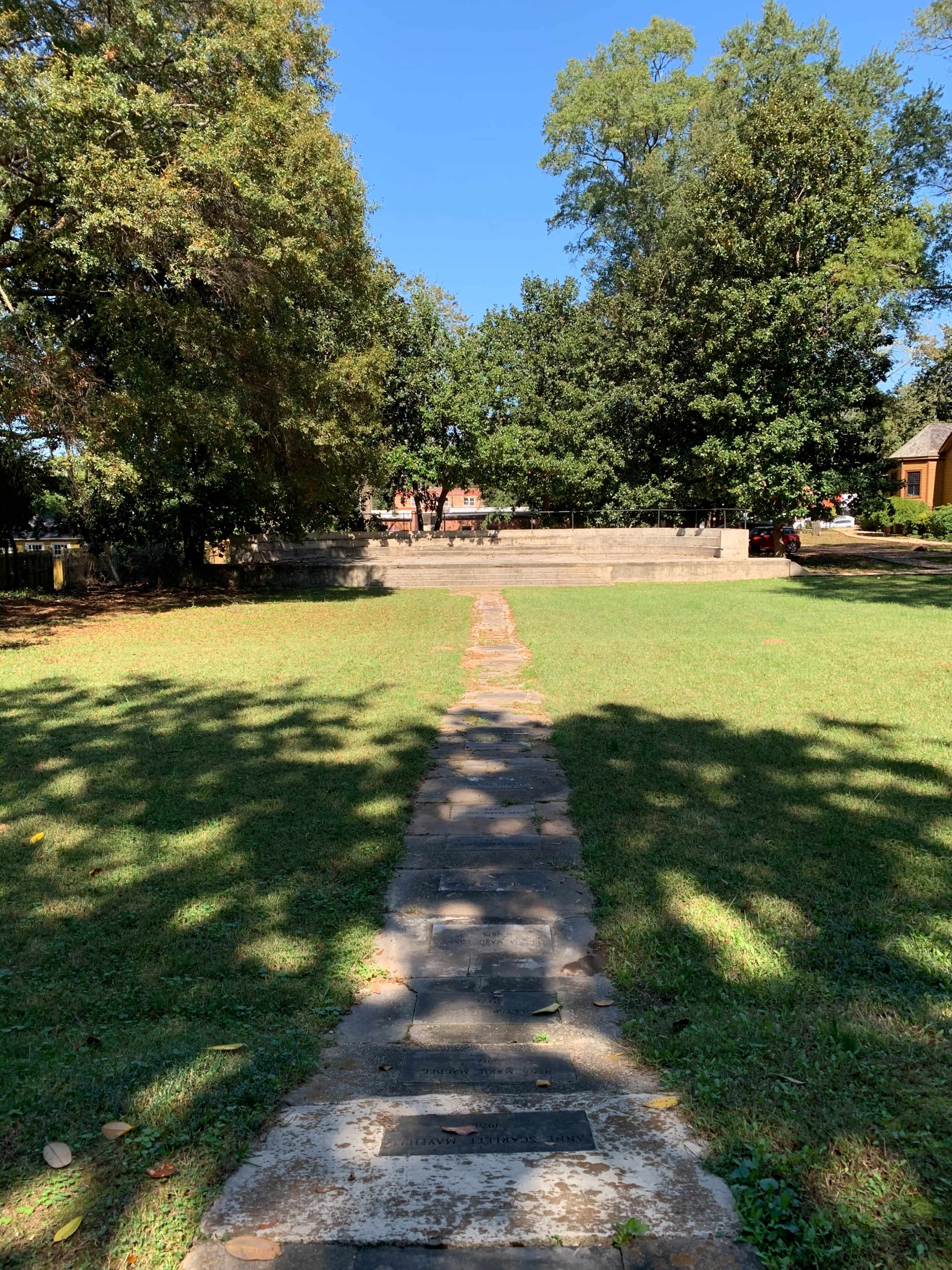 A stone pathway leads through a grassy area toward a small stone structure surrounded by trees.
