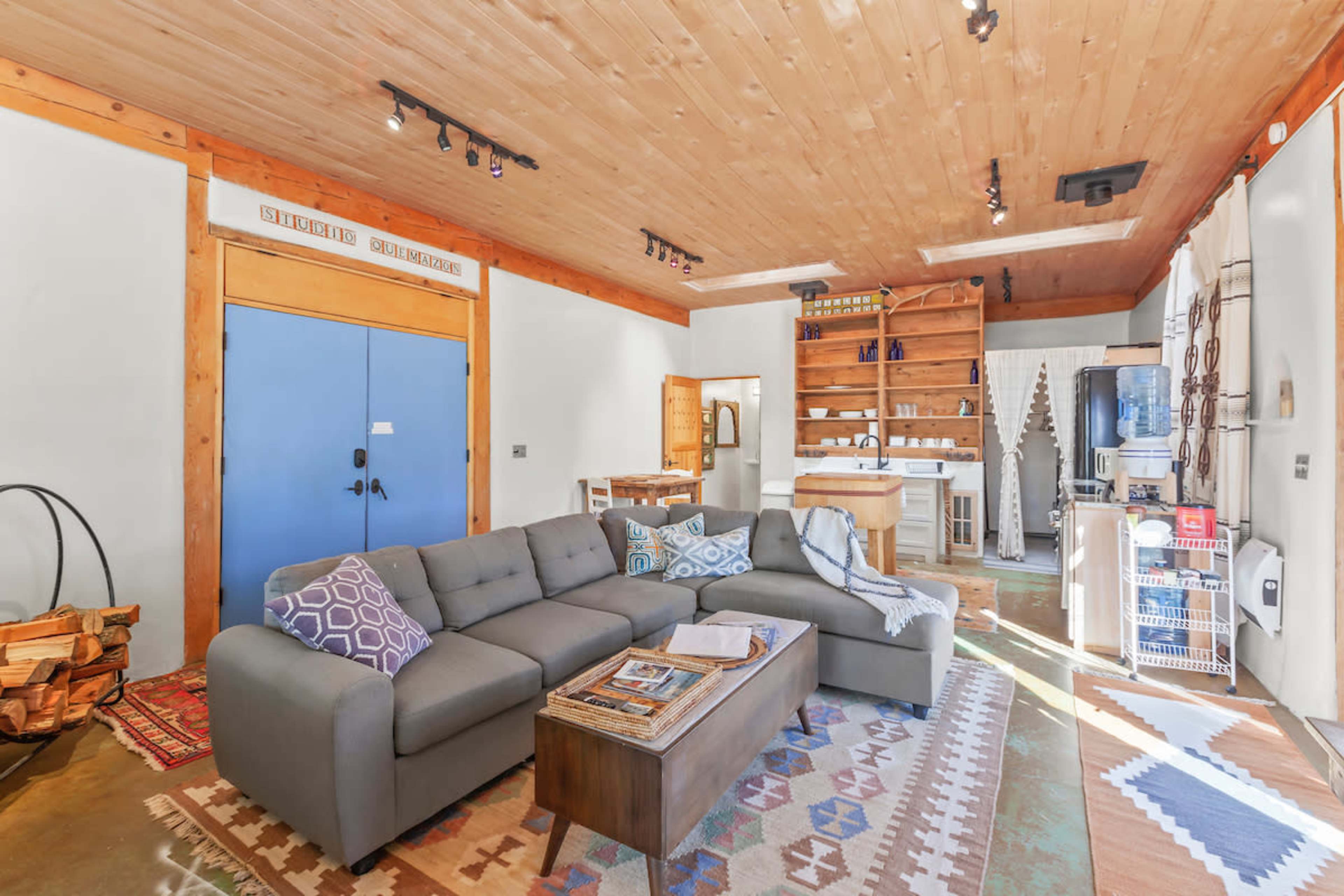 A cozy living area with a large gray sectional sofa, a wooden coffee table, shelves filled with items, and a rustic wood ceiling.