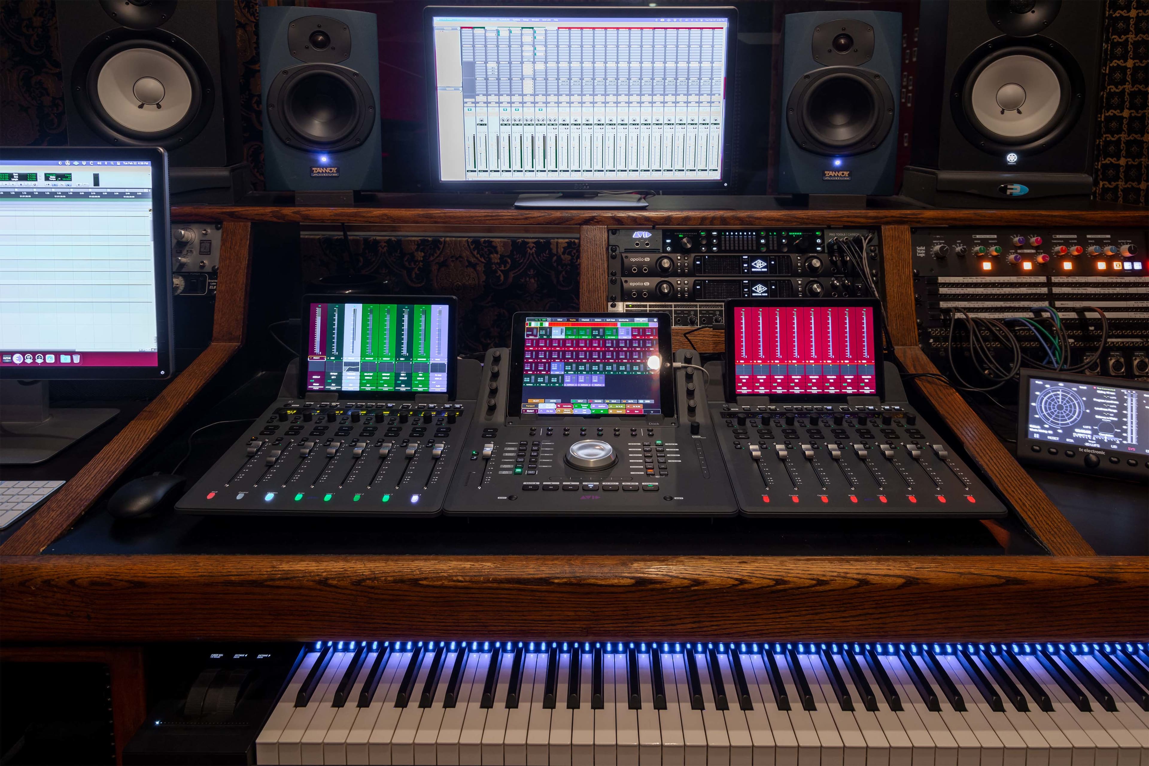 A music production setup featuring digital audio workstations, mixing consoles, studio monitors, and a MIDI keyboard.