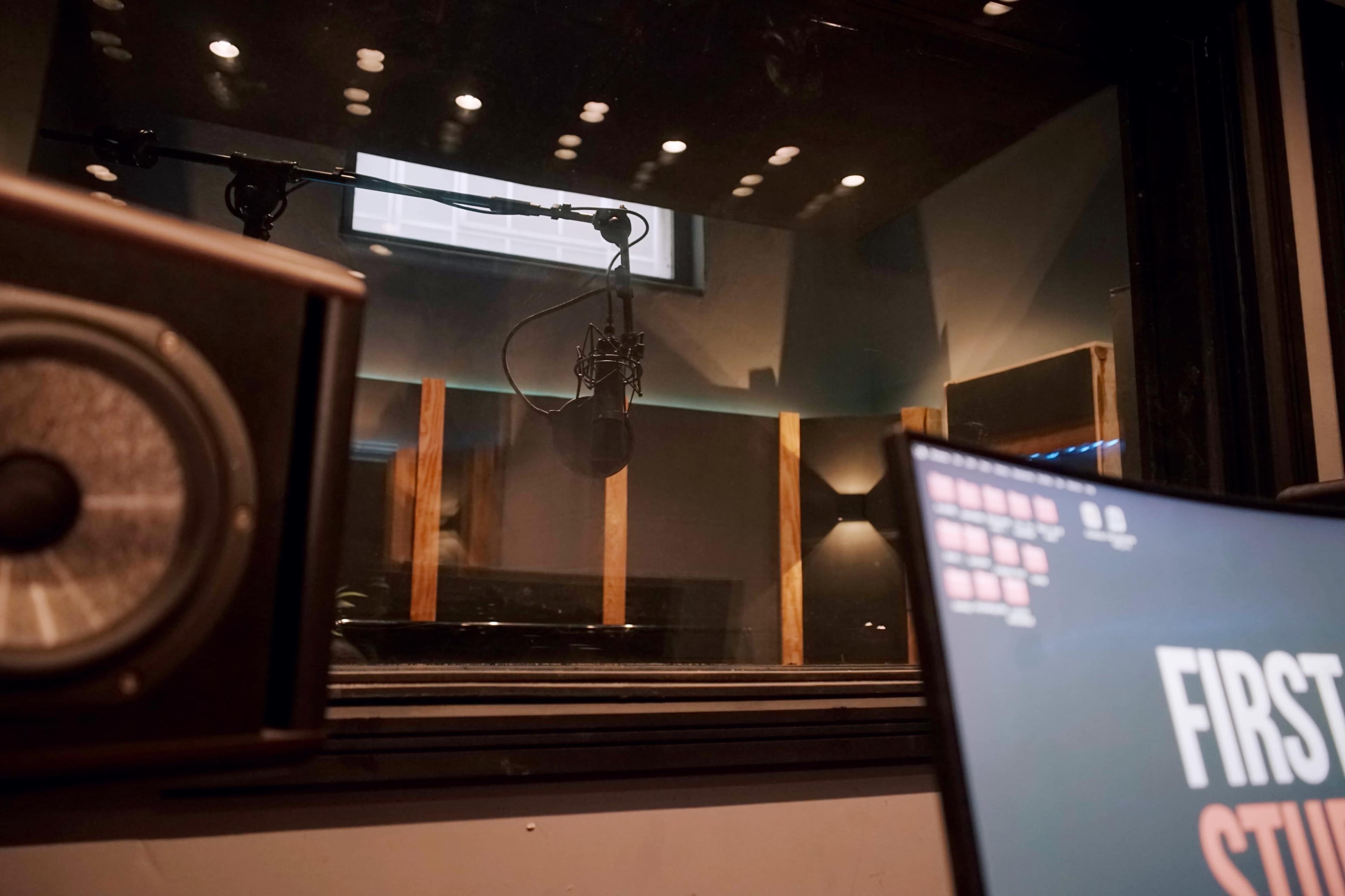 The image shows a sound recording studio with a microphone suspended from the ceiling and audio equipment visible in the foreground.