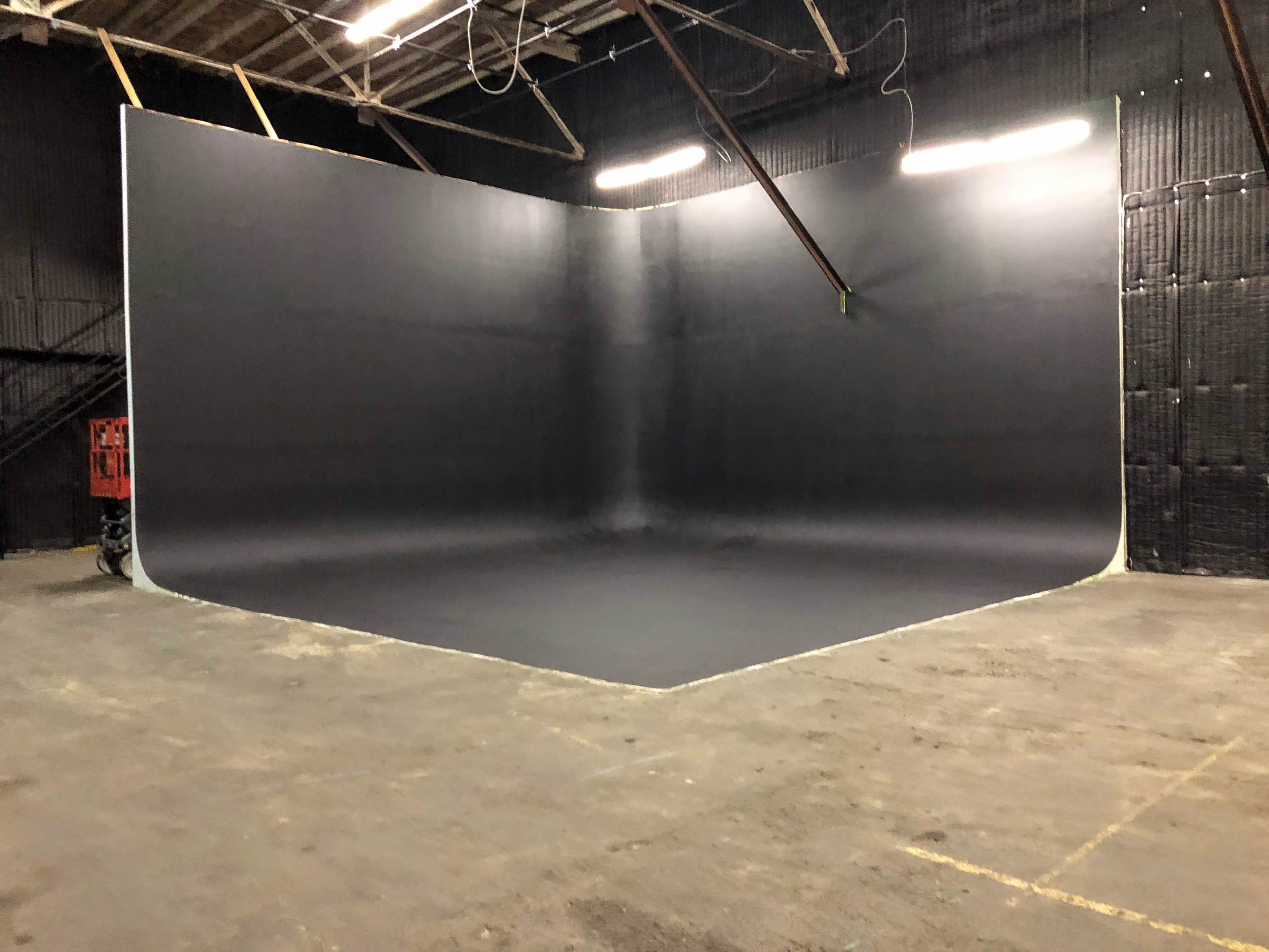 The image shows a spacious photography studio with a large, flat, black backdrop in one corner.