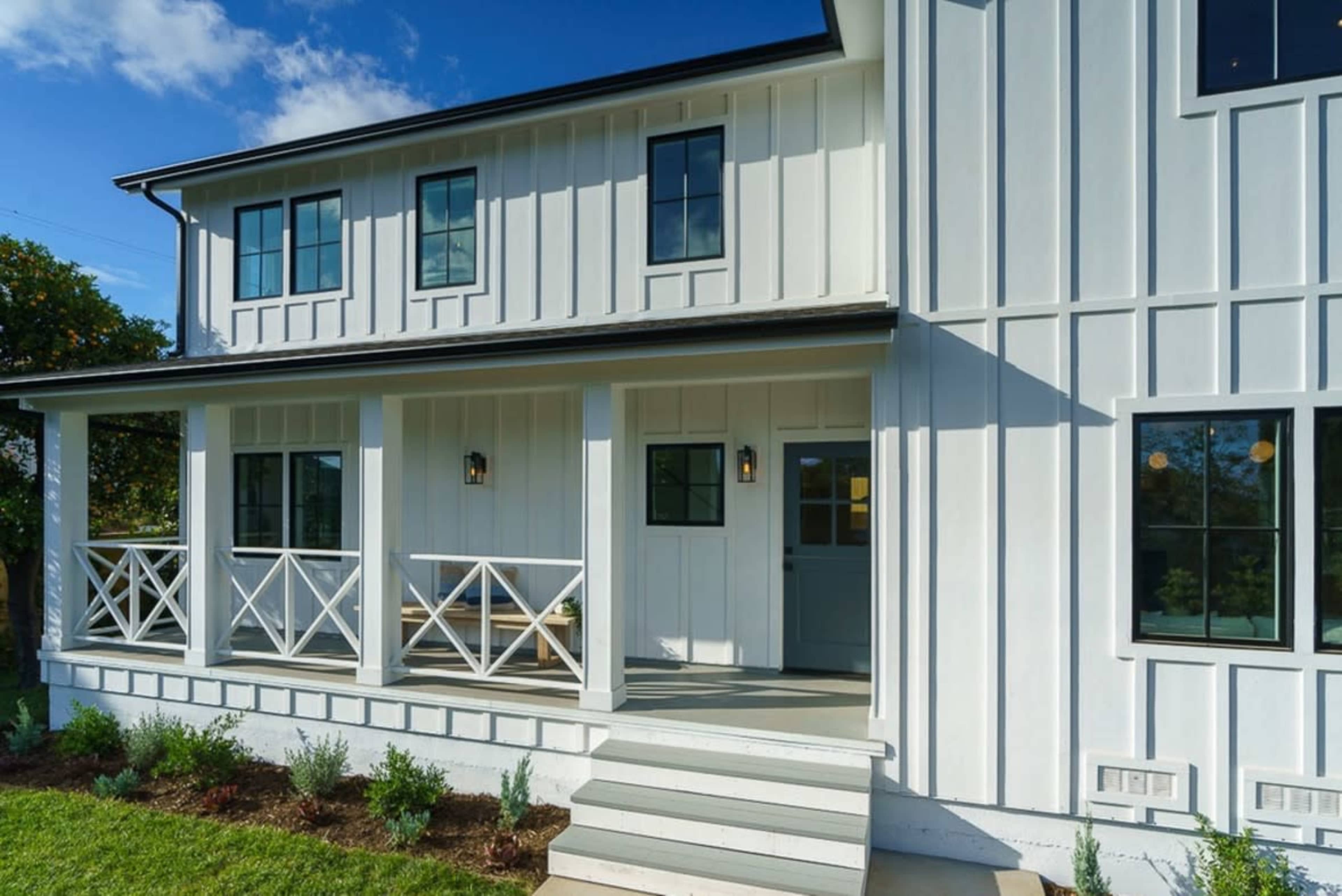 A two-story white house features a front porch with a railing and large windows.