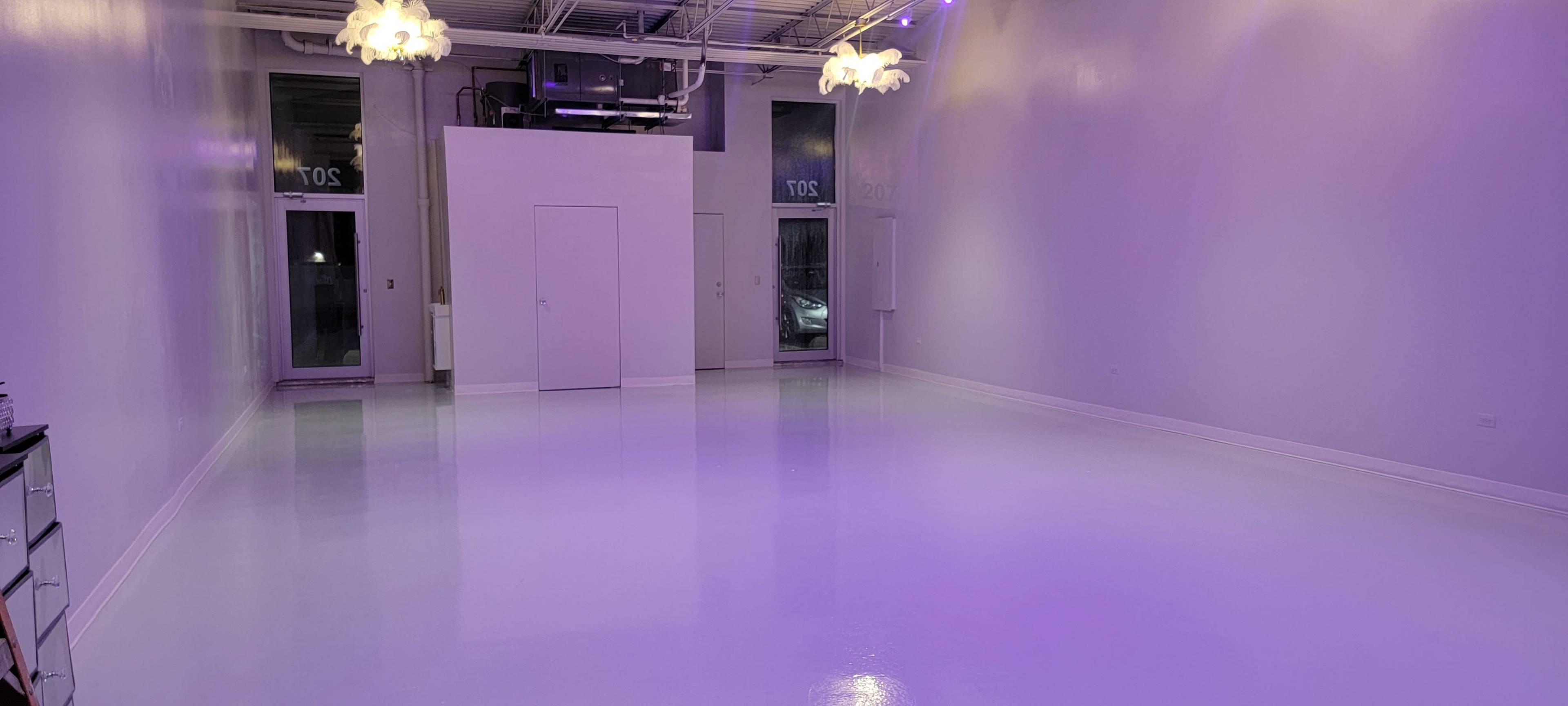 The image shows a spacious, empty room with glossy white flooring and soft purple lighting, featuring two doors on one side.