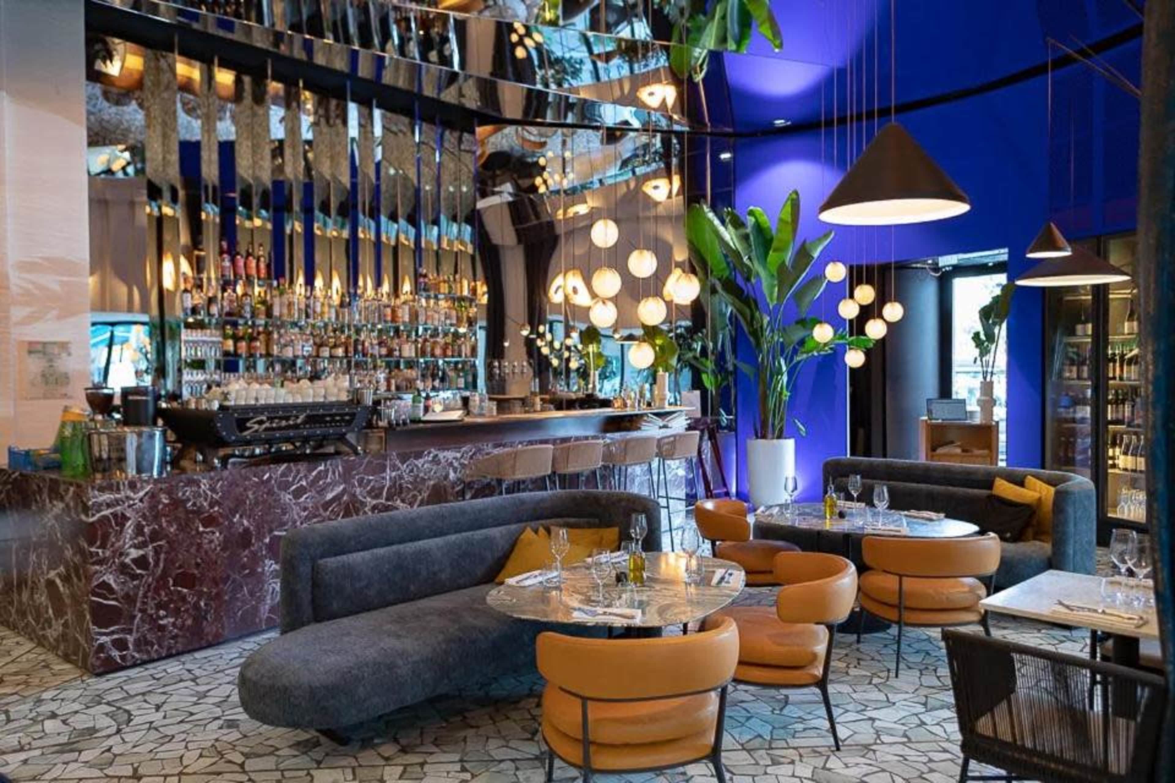 A modern restaurant interior featuring a bar with a mirrored backdrop, curved seating arrangements, and pendant lighting.