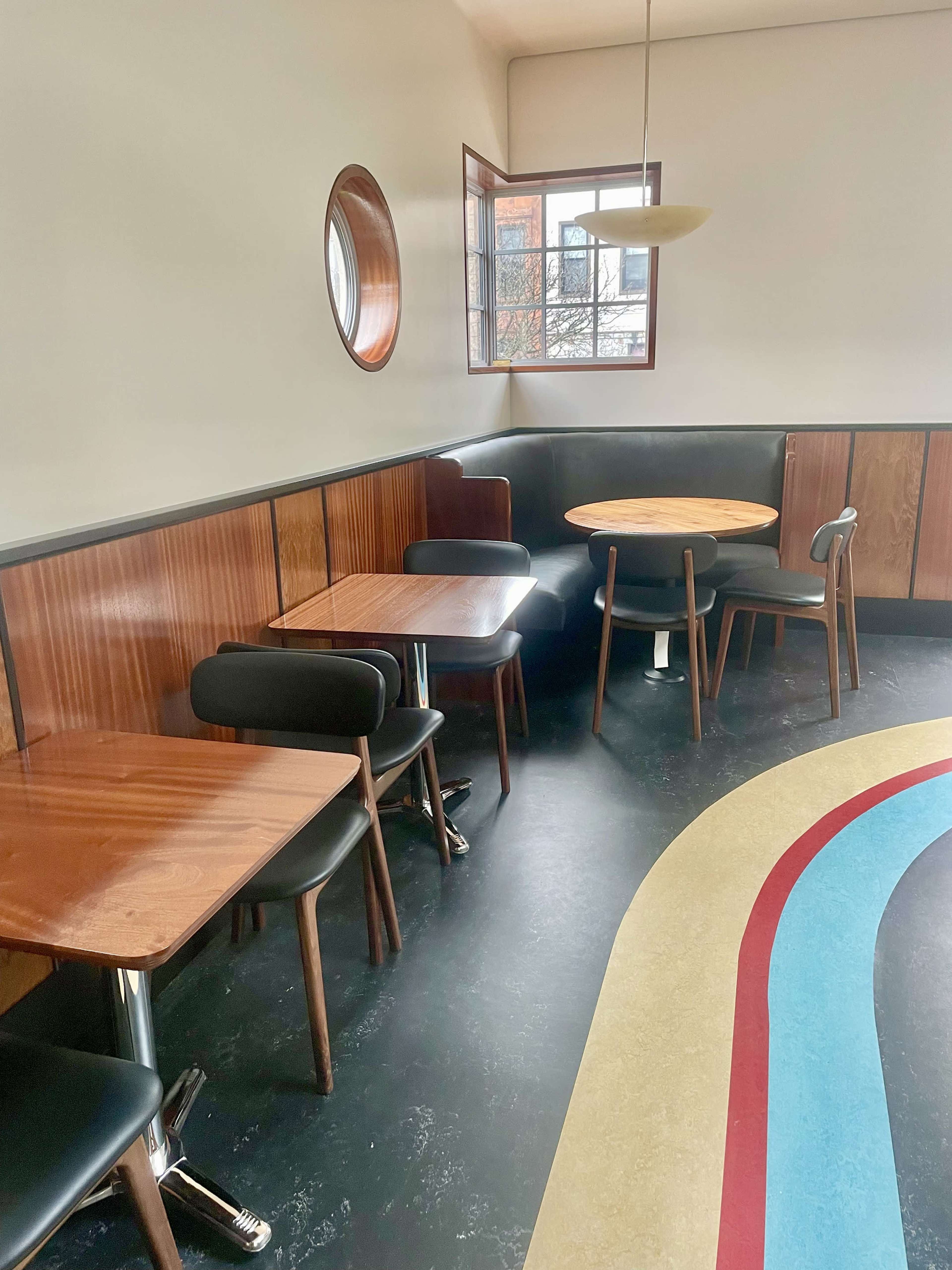 A minimalist café interior featuring wooden tables and chairs arranged around a colorful curved floor design.