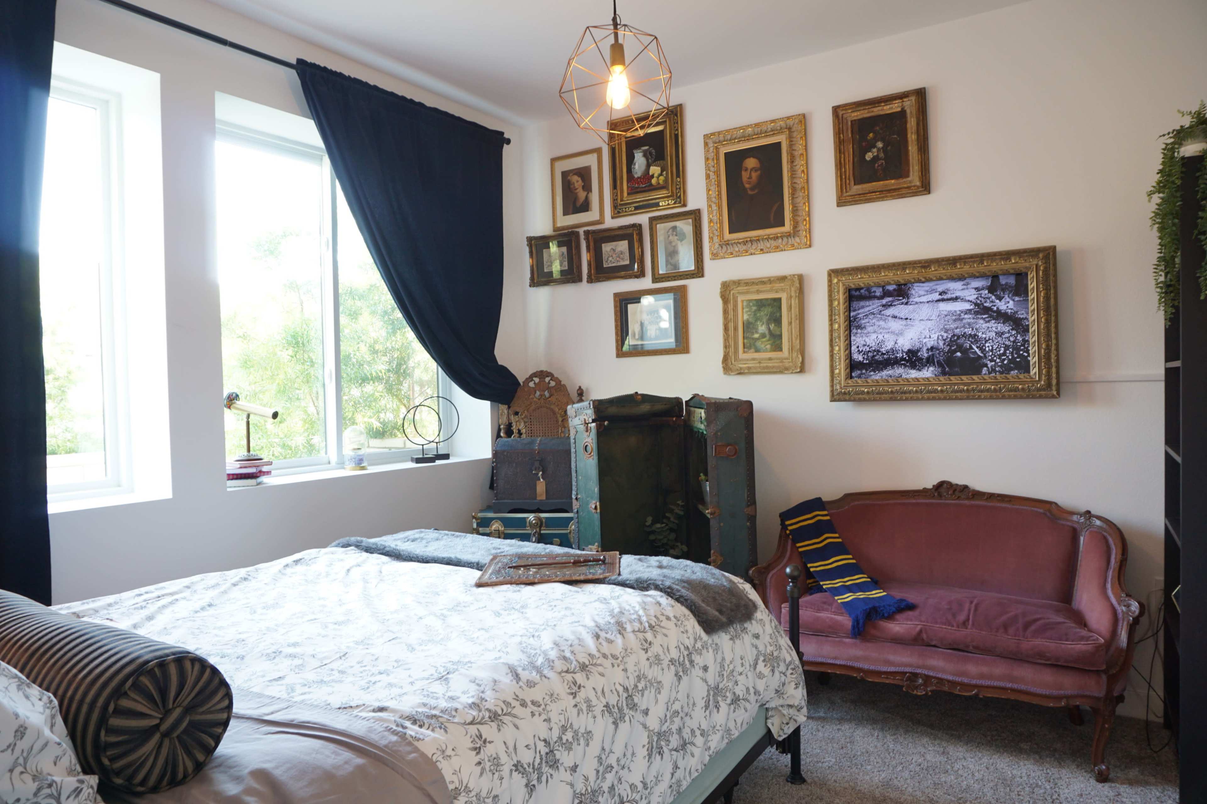 The room features a bed with a patterned comforter, a vintage-style pink sofa, and a wall adorned with framed artwork and photographs.