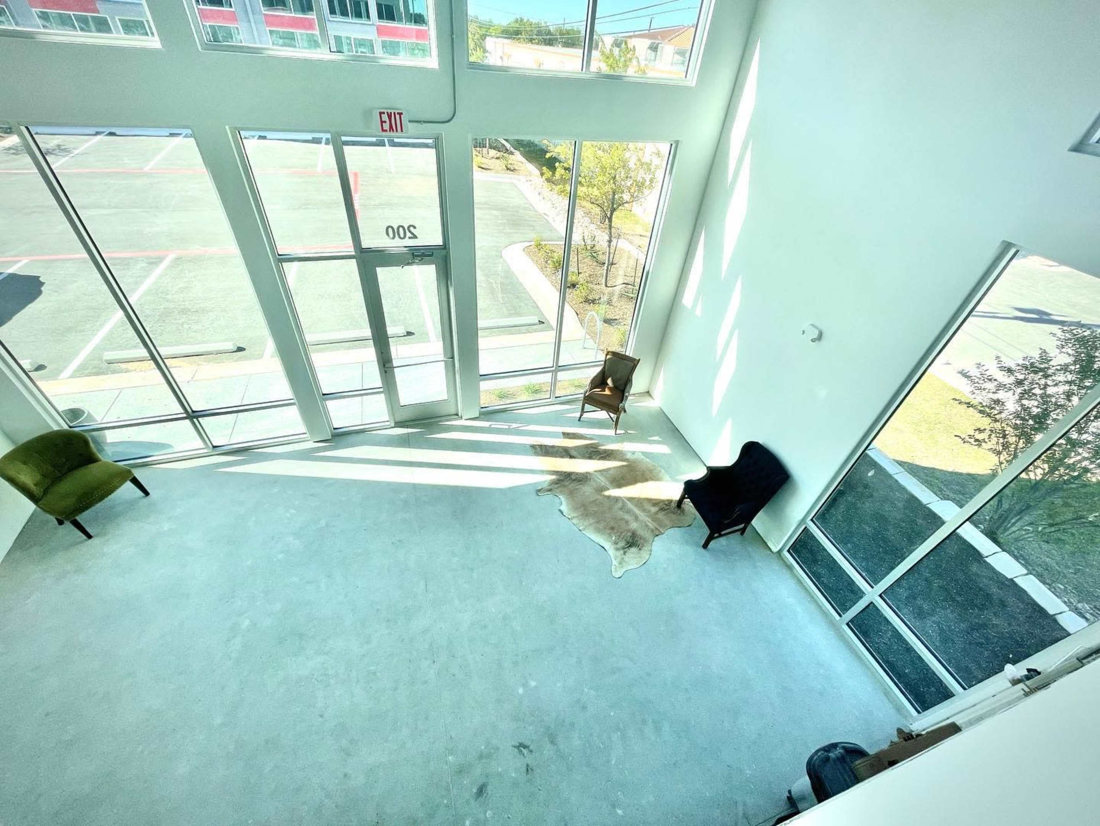 A spacious, airy room with large windows, two chairs, and a cowhide rug on the concrete floor.