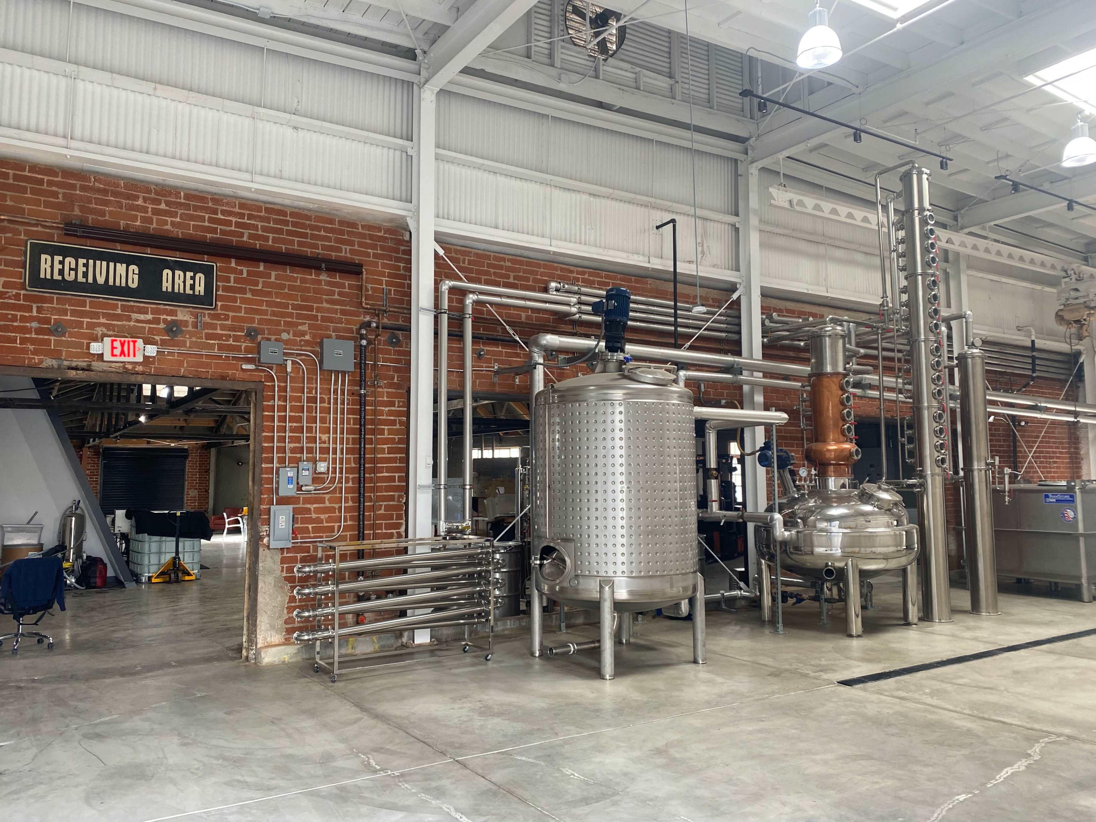 A distillation area featuring stainless steel equipment and pipes, with a sign indicating "RECEIVING AREA" on the wall.