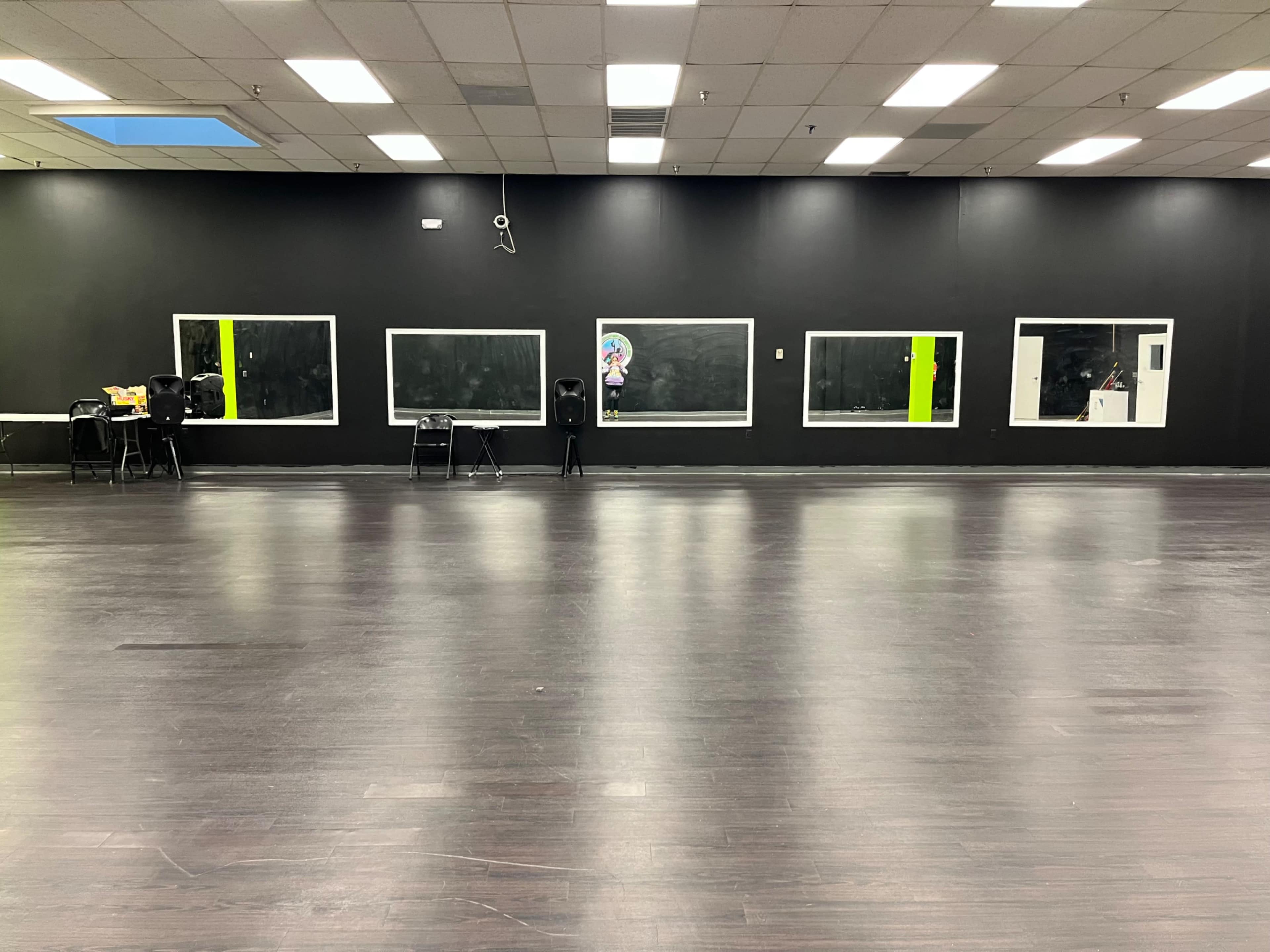 A large, empty dance studio with dark walls, wooden floors, and several mirrors.