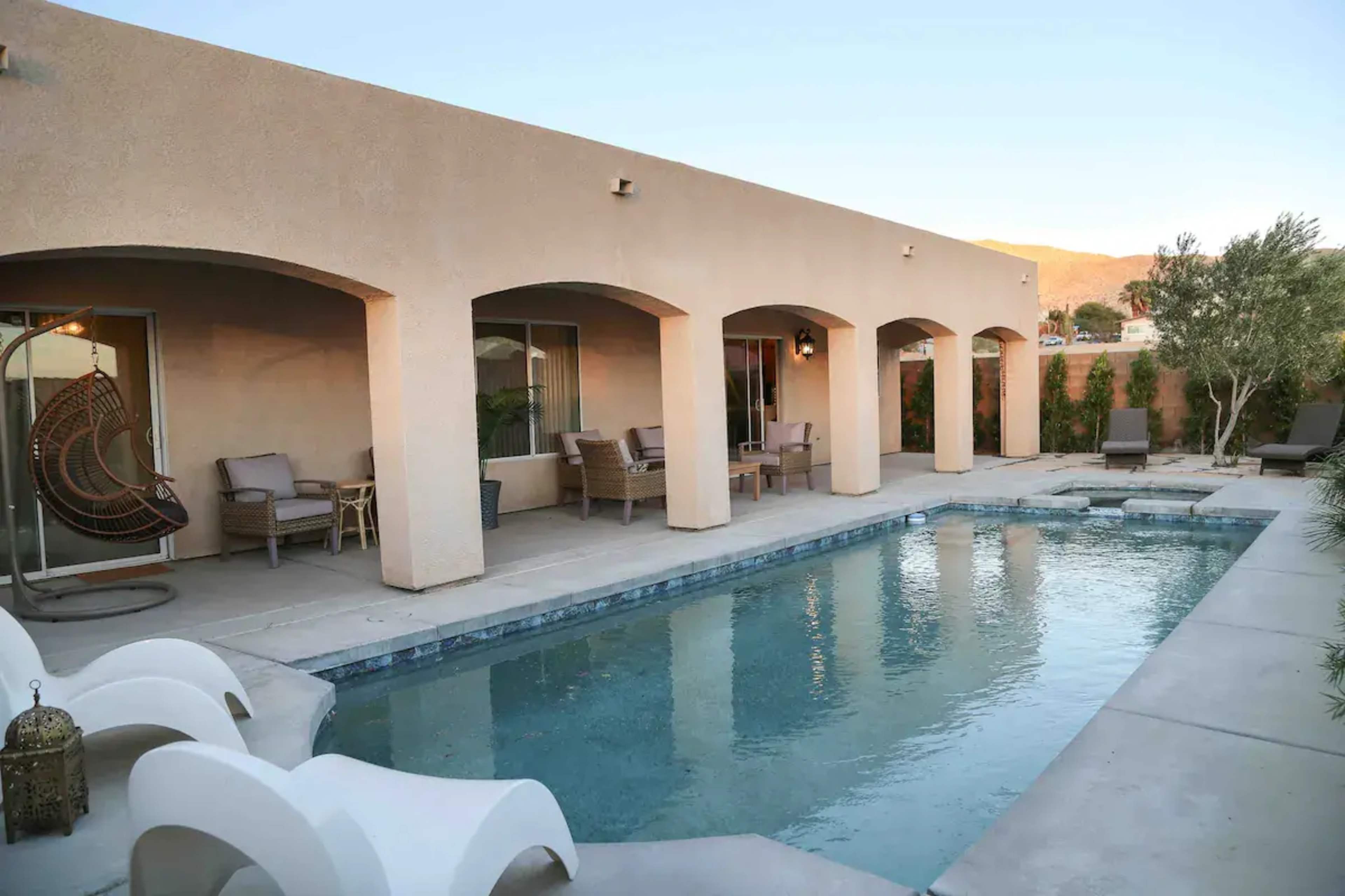 The image shows a backyard with a swimming pool surrounded by seating areas and a stucco wall, set against a mountainous backdrop.