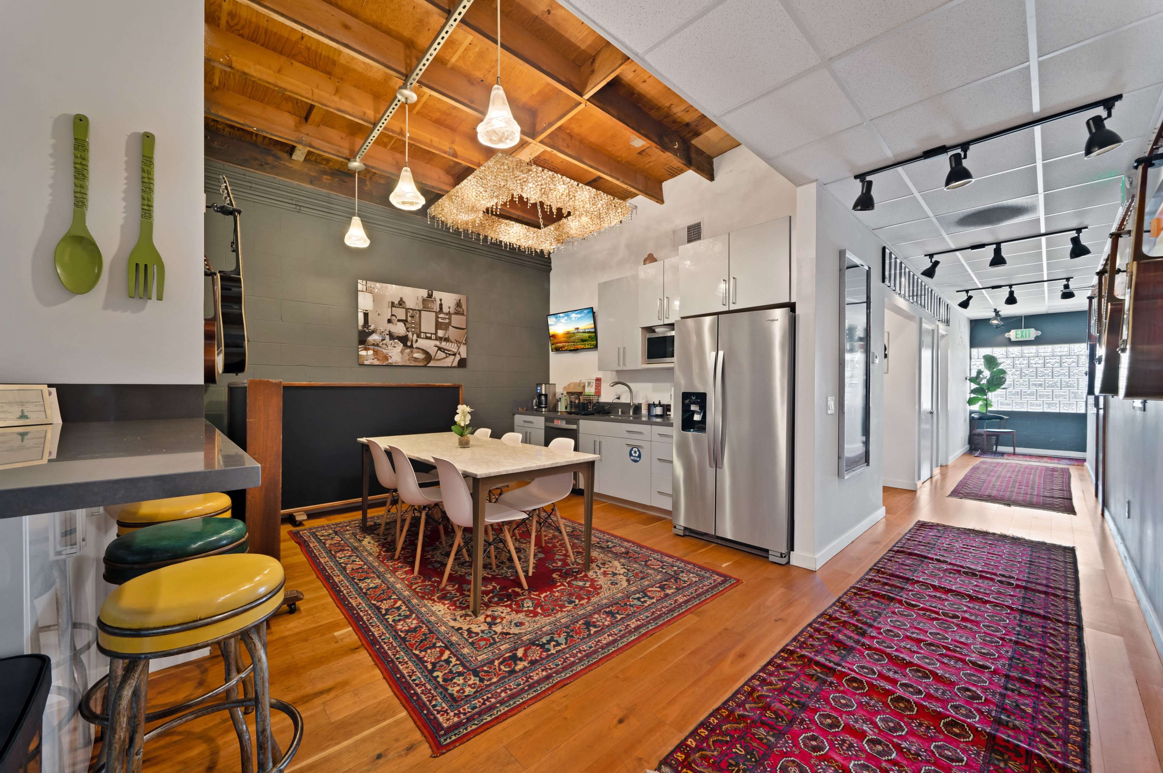 A well-lit kitchen and dining area with a wooden table, modern appliances, and a hallway leading to additional rooms, featuring a decorative rug.