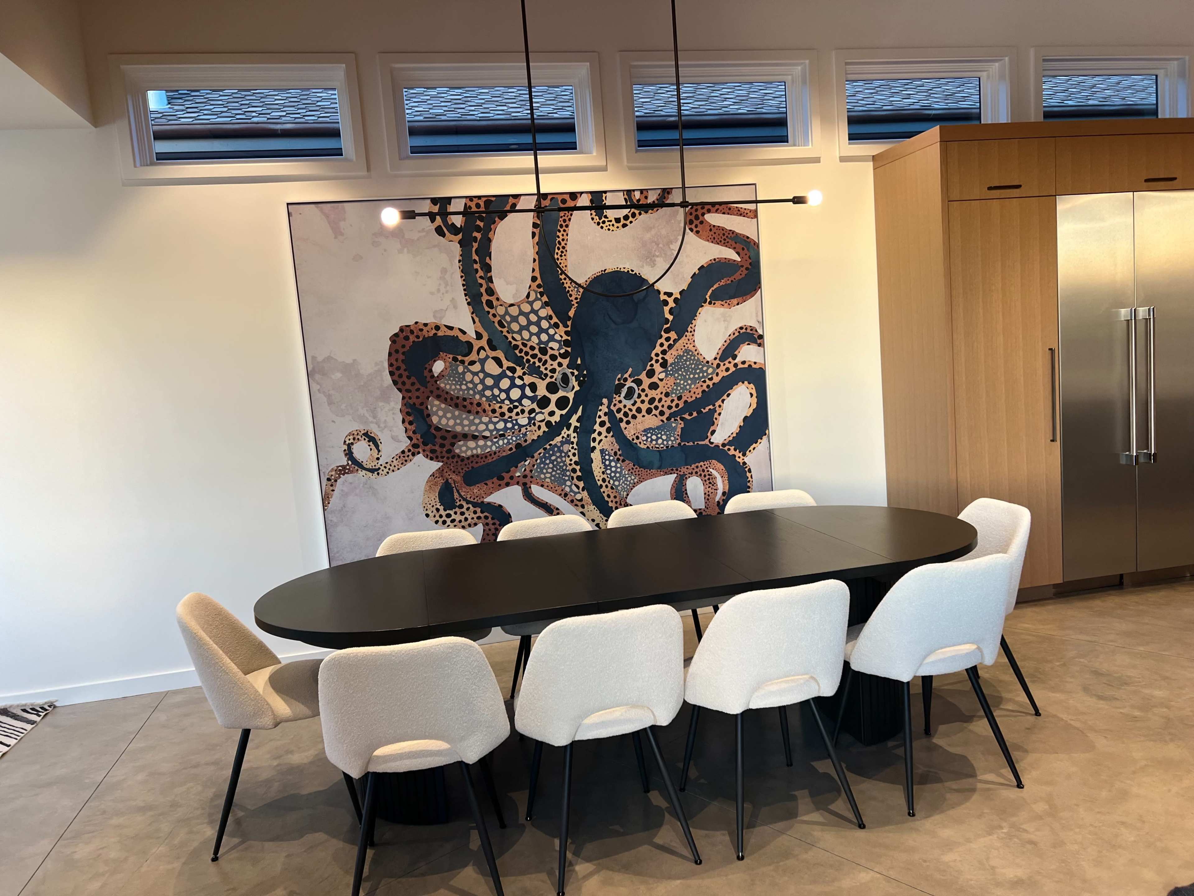 The image shows a dining area with a large oval black table surrounded by white upholstered chairs, and an artistic octopus mural on the wall behind it.