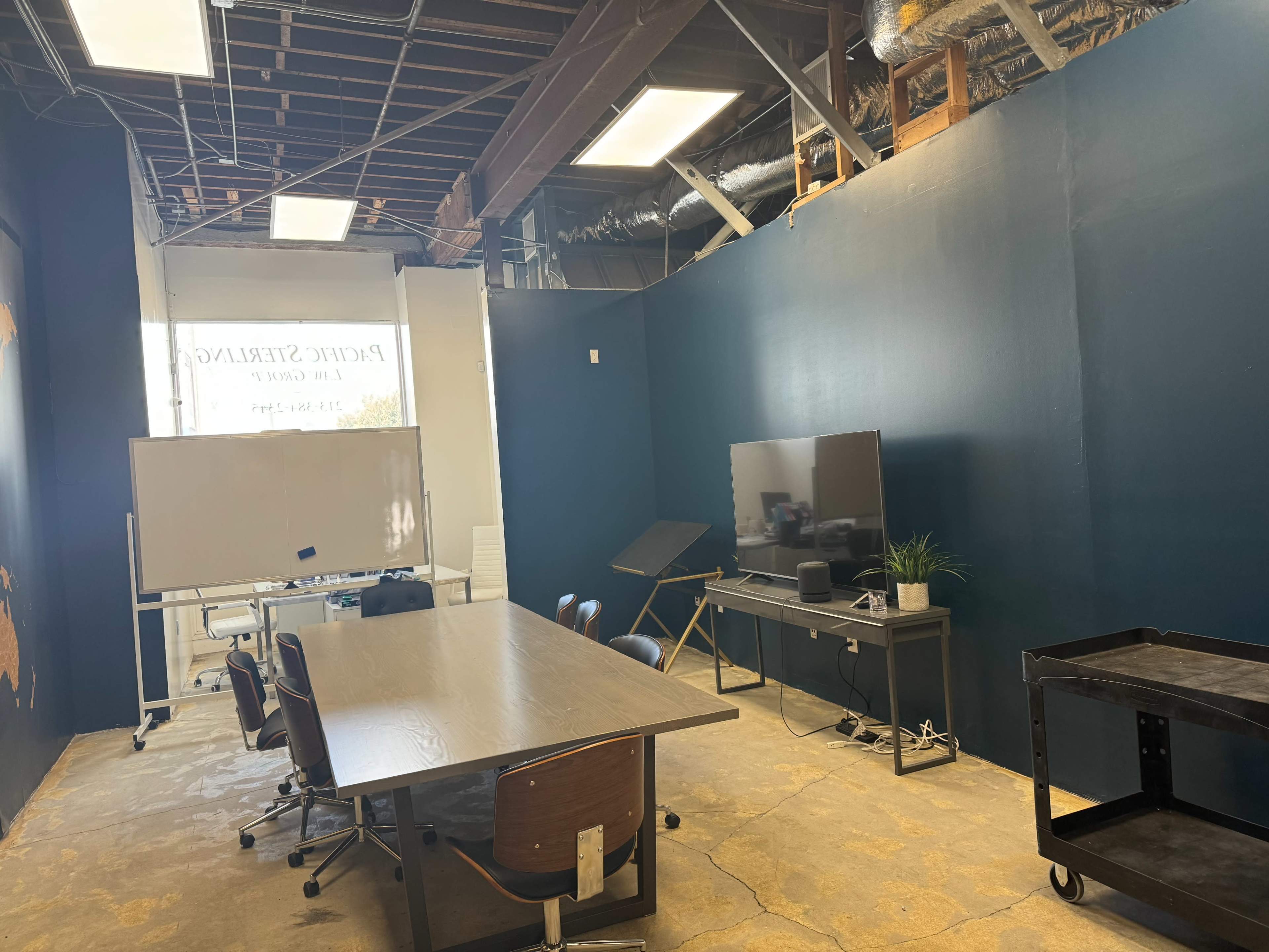 A meeting room with a large table, chairs, a whiteboard, a television, and exposed ceiling structures.