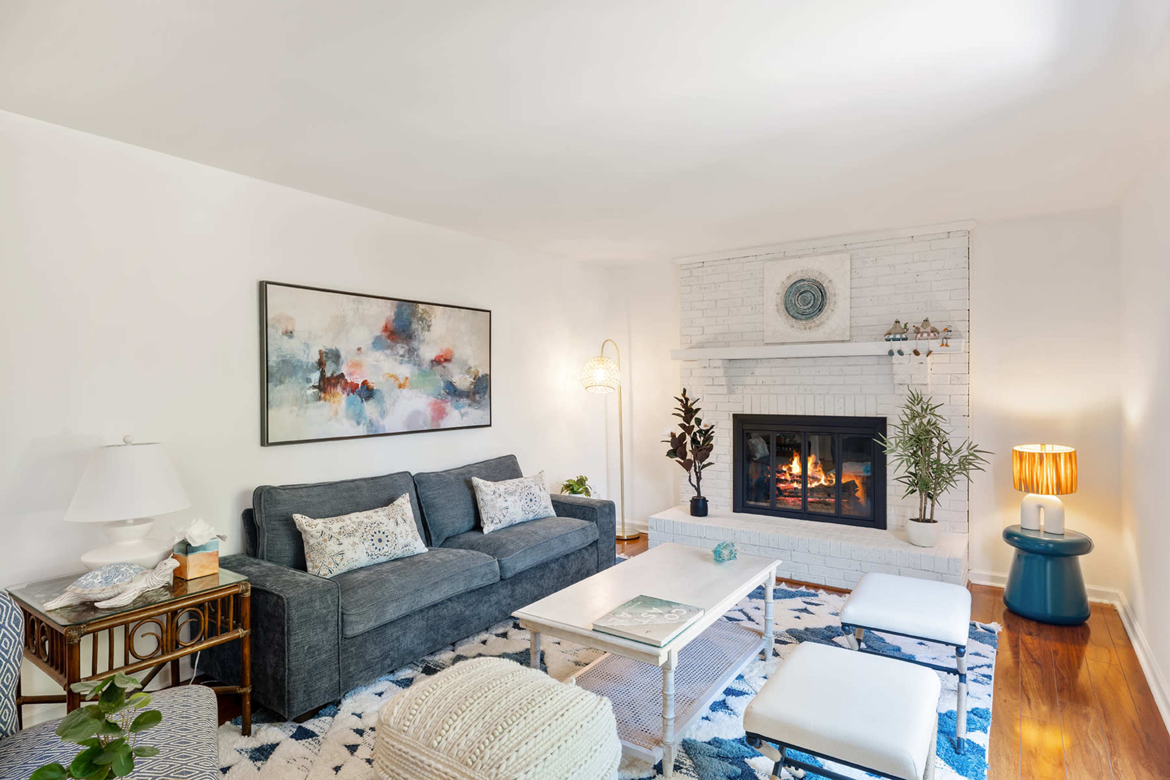 A cozy living room features a gray sofa, a white brick fireplace, and a decorative coffee table with a large area rug underneath.