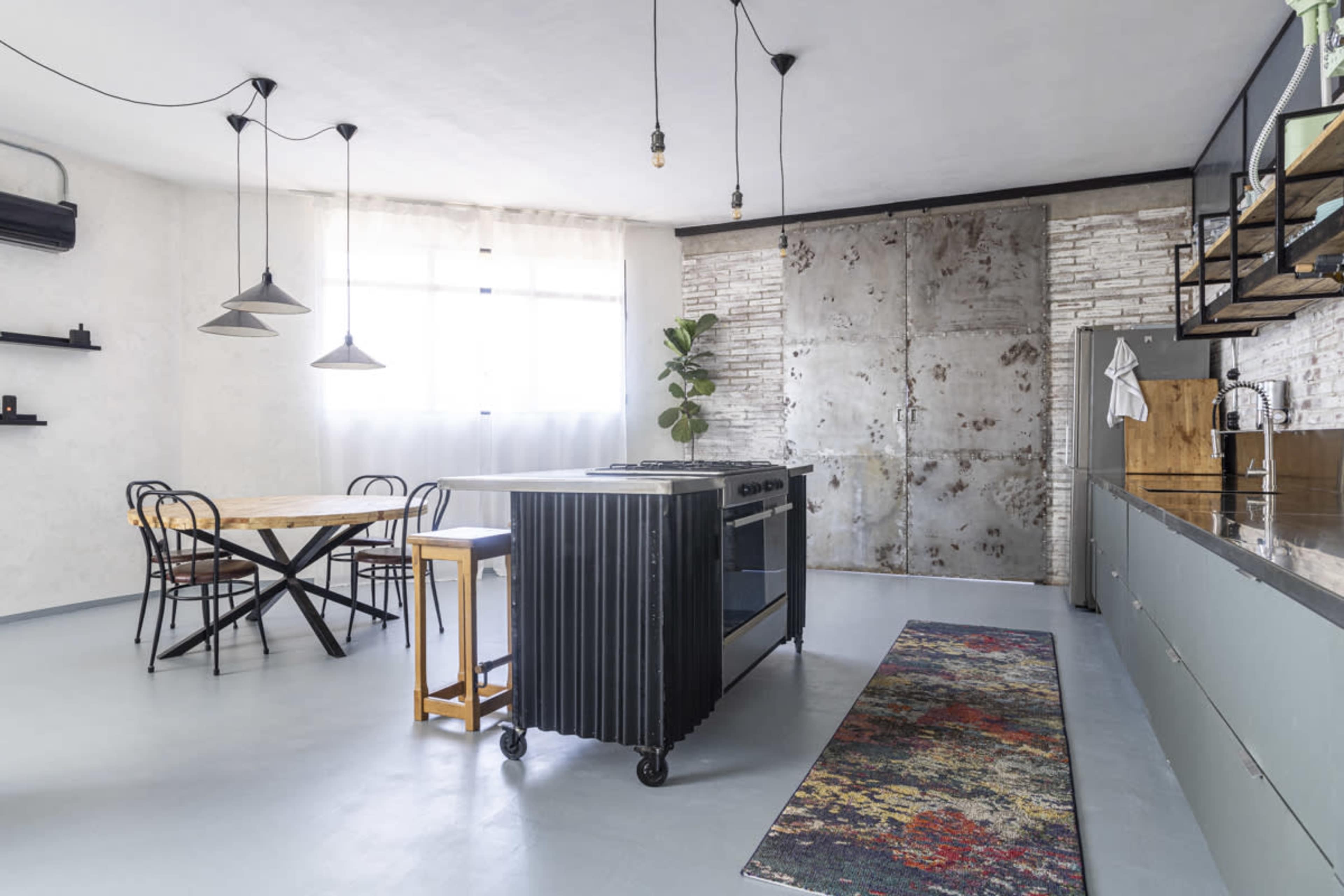 The image shows a modern kitchen featuring a central island with a stove, a wooden dining table, and a large metal sliding door.