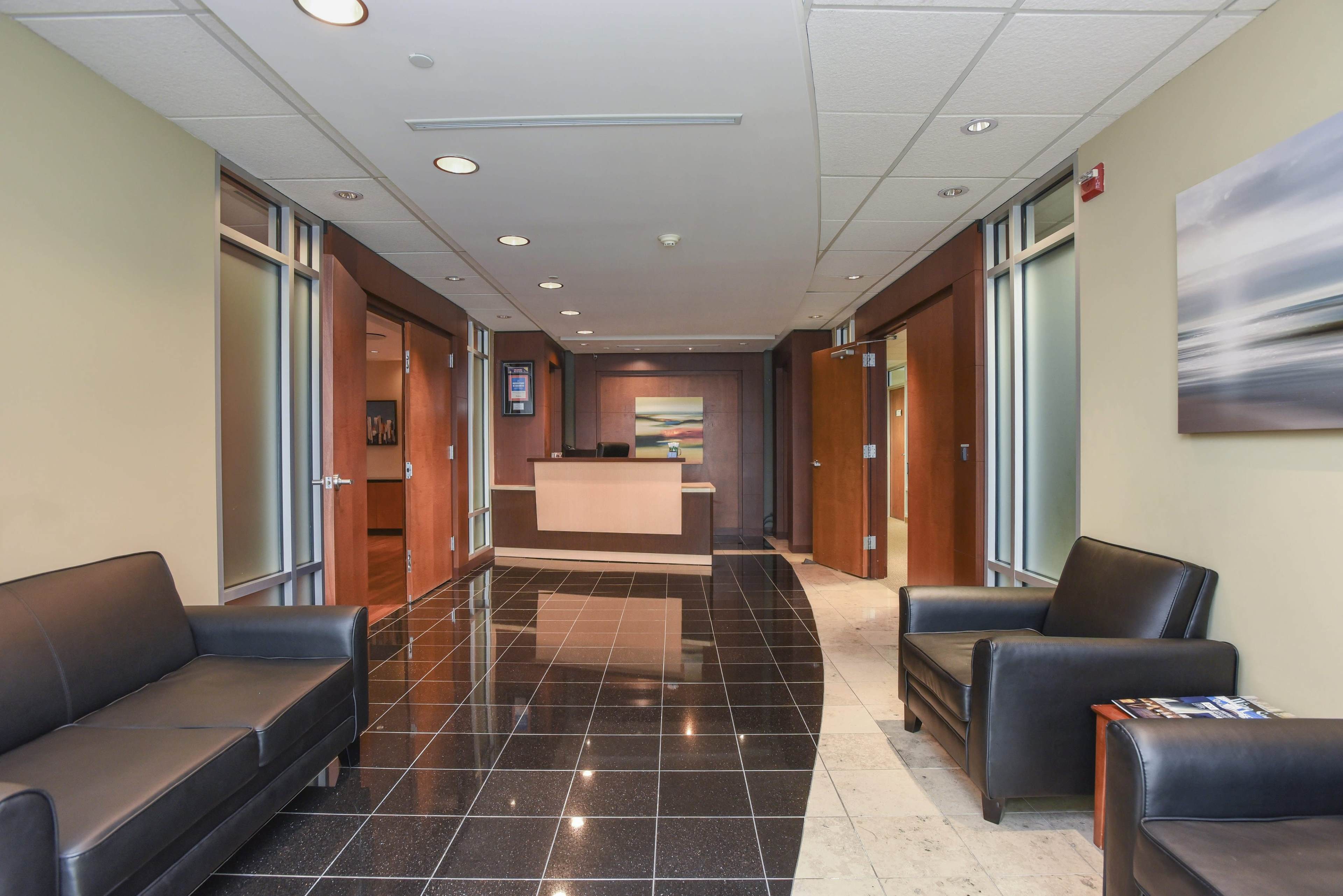 A modern reception area with black tiled floors, leather seating, and a wooden reception desk in the background.