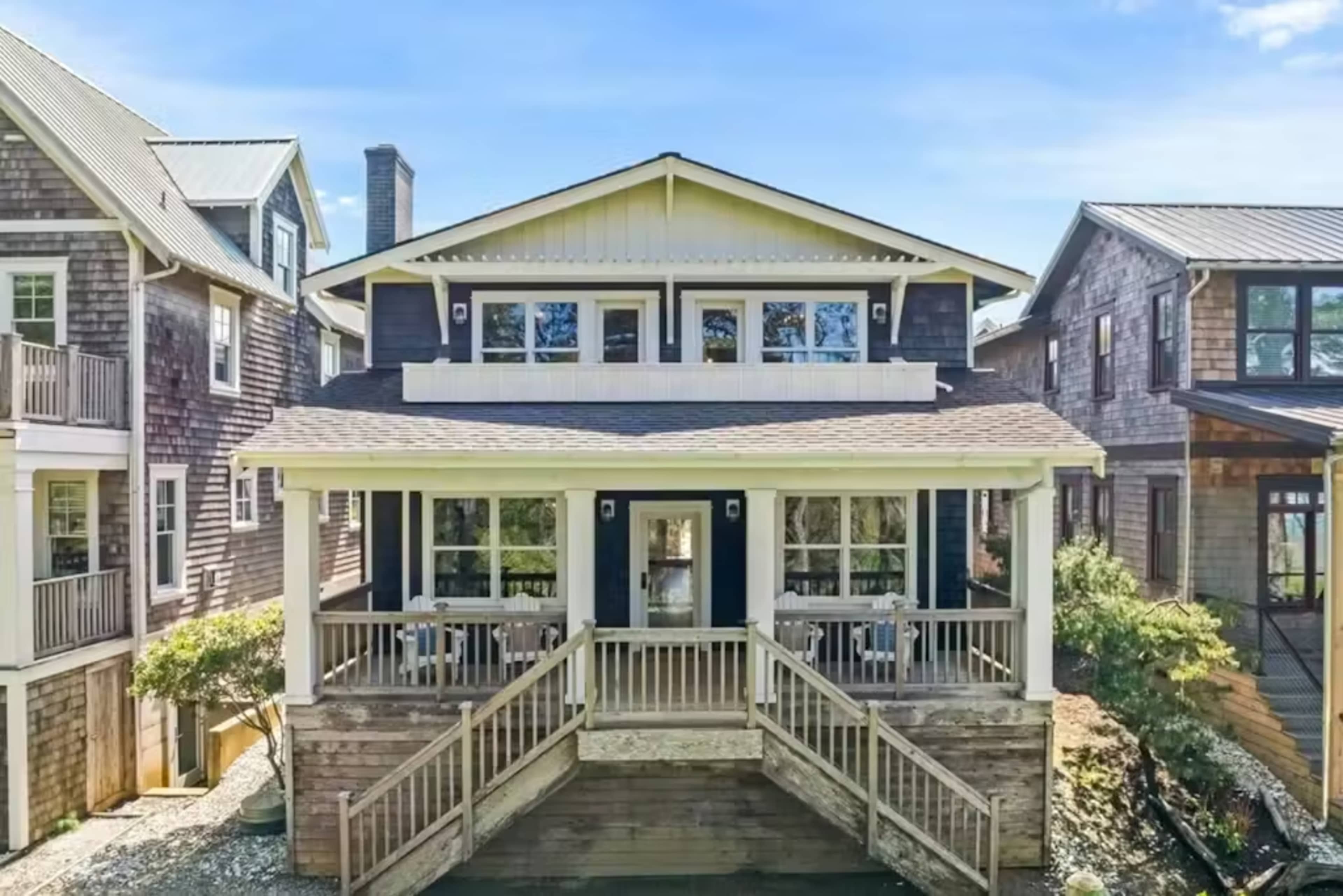 The image shows a large, multi-story wooden house with a wide front porch and multiple windows, surrounded by other similar homes in a residential area.