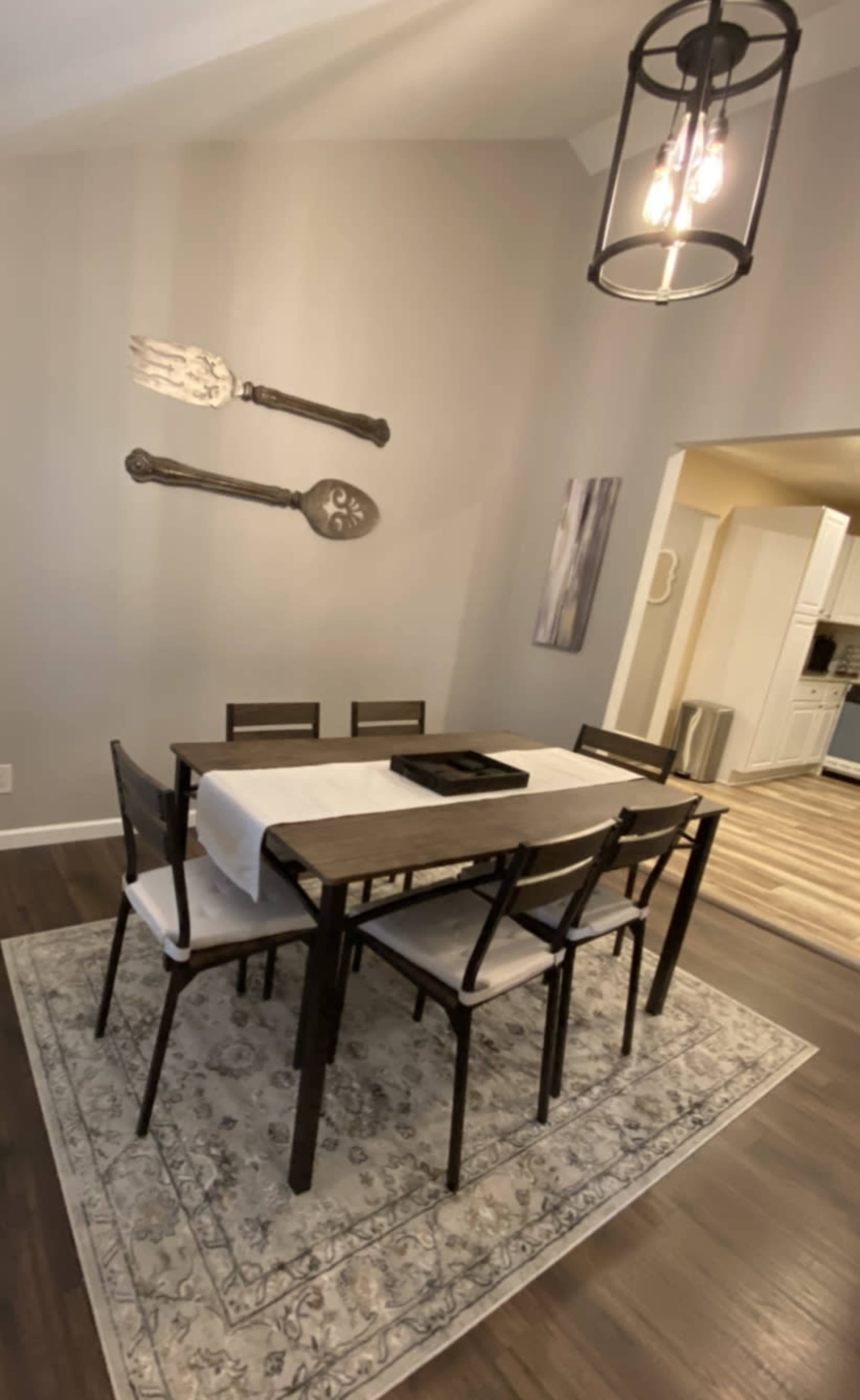 A rectangular dining table surrounded by six chairs is positioned on a decorative rug in a light-colored dining area.