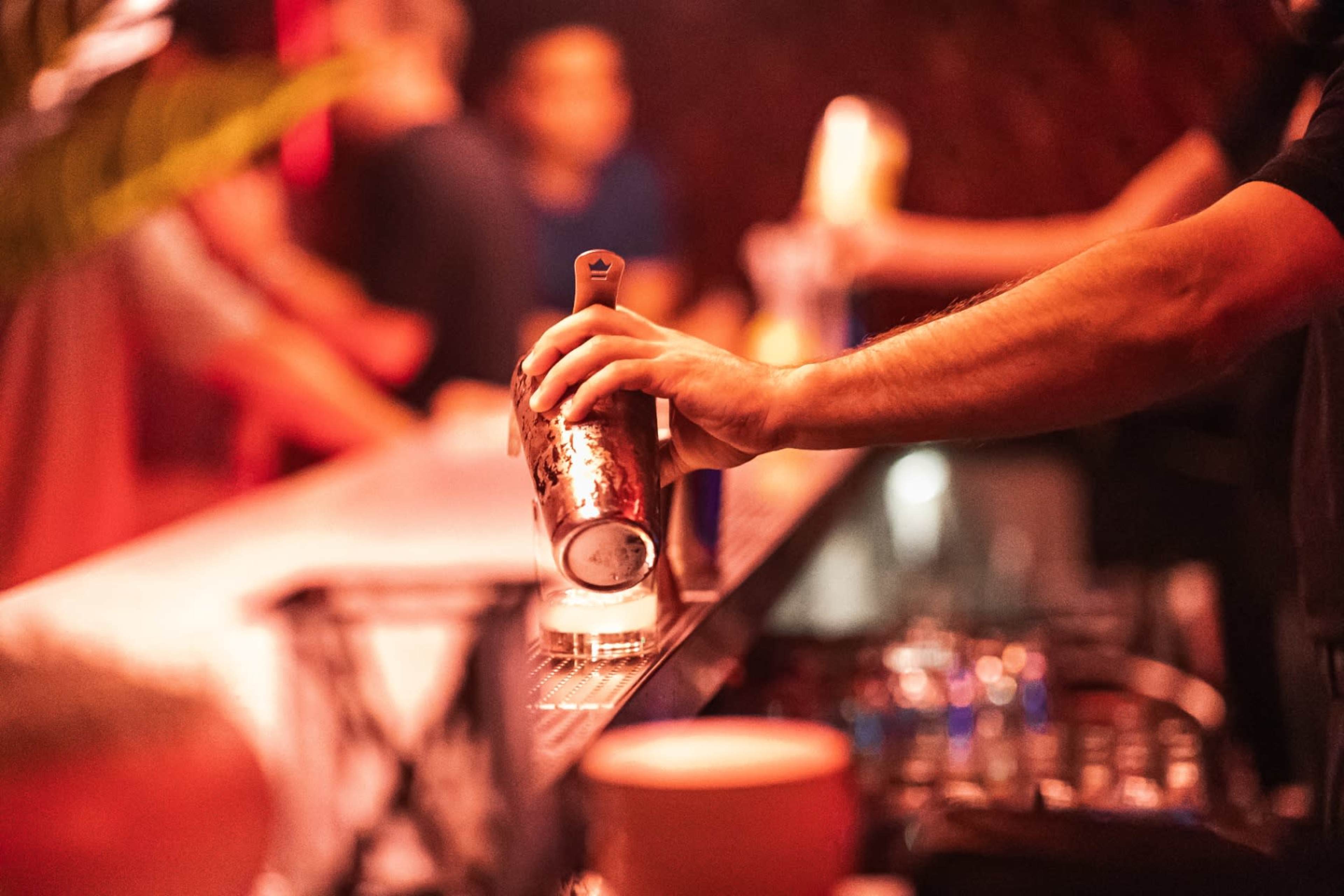 A bartender is pouring a drink from a shaker into a glass at a dimly lit bar.