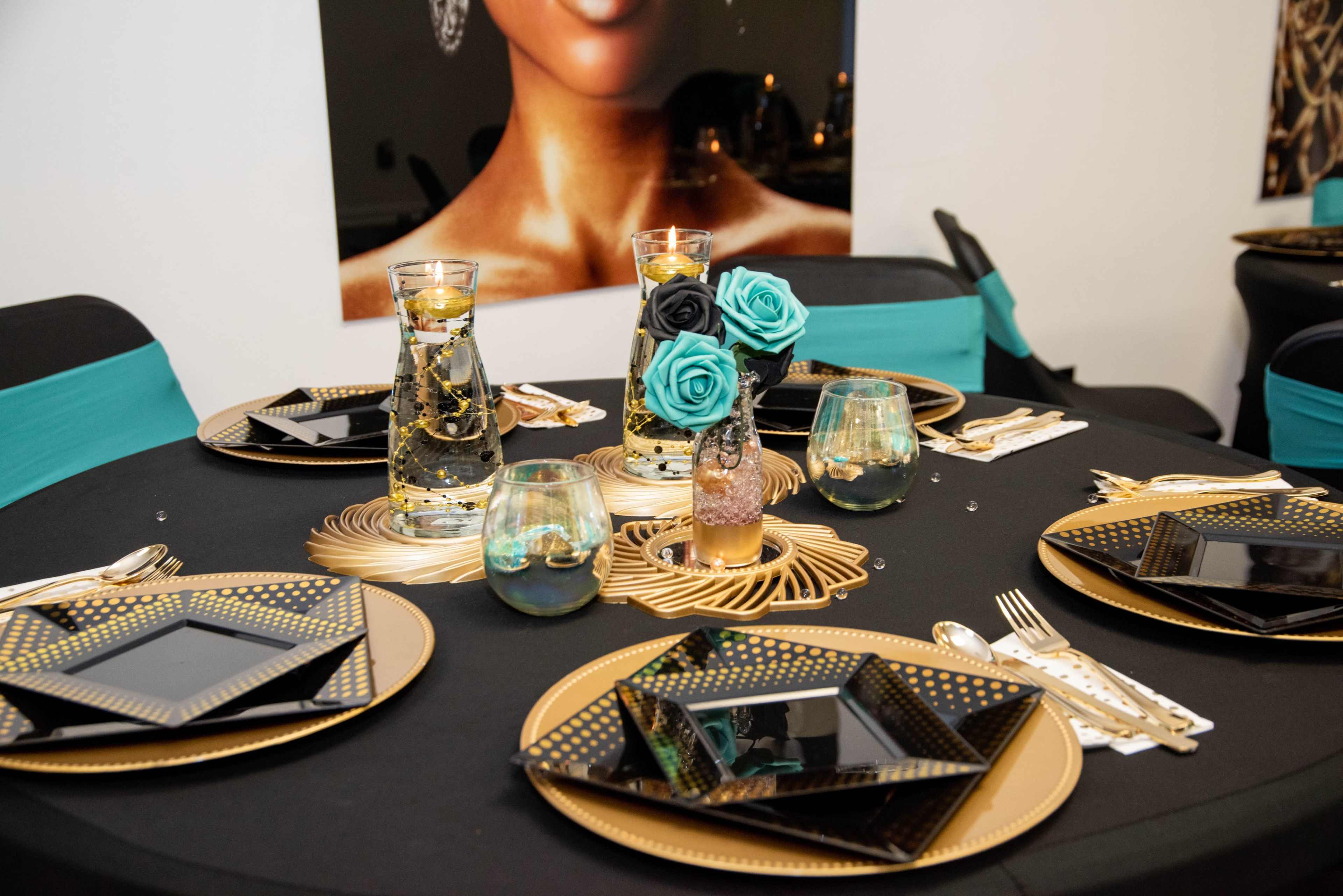 A table set for a formal event with black and gold dinnerware, decorative glasses, and floral accents.