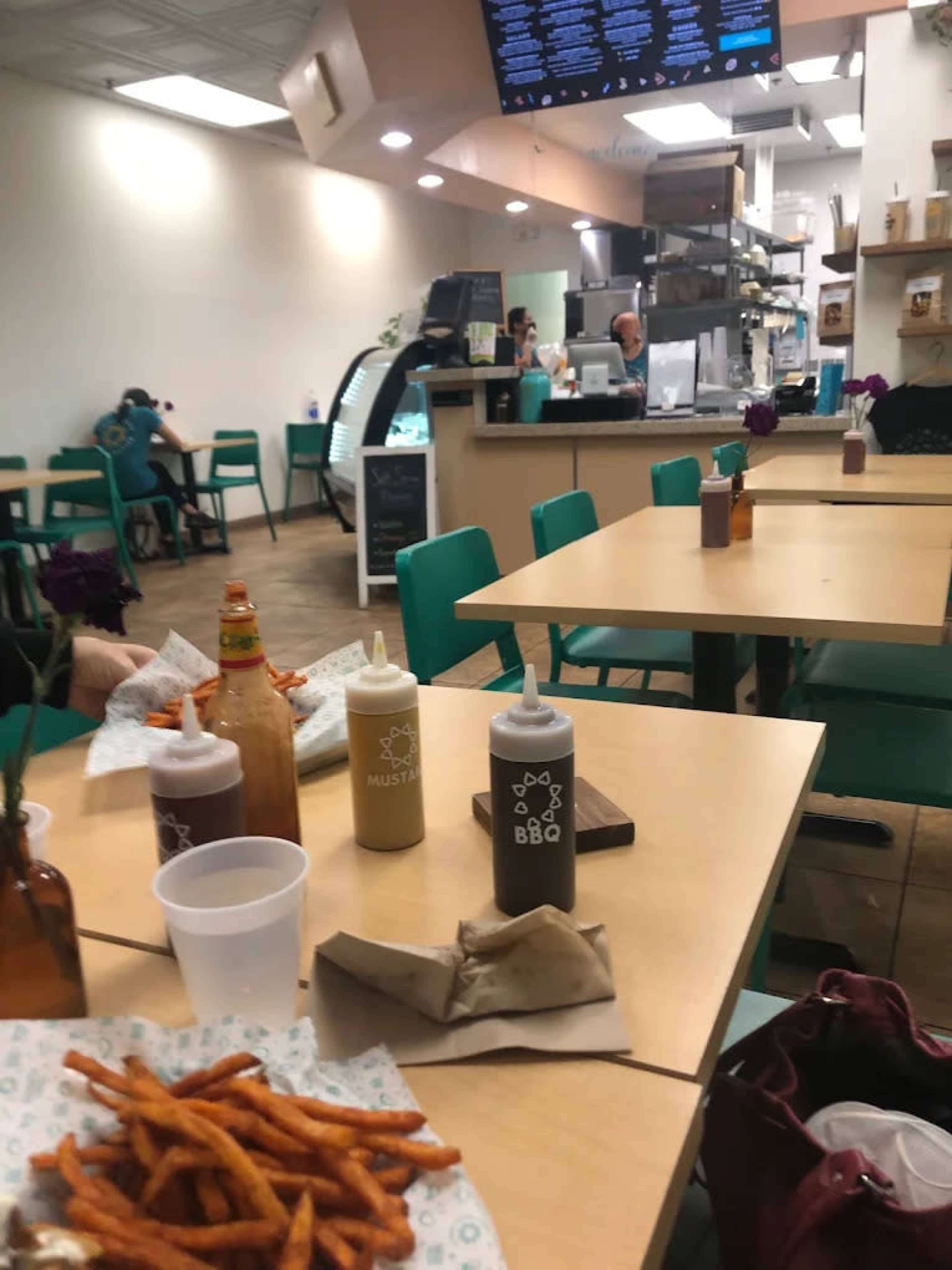 A casual dining area with empty tables, condiment bottles, and a view of the kitchen, along with a plate of sweet potato fries in the foreground.