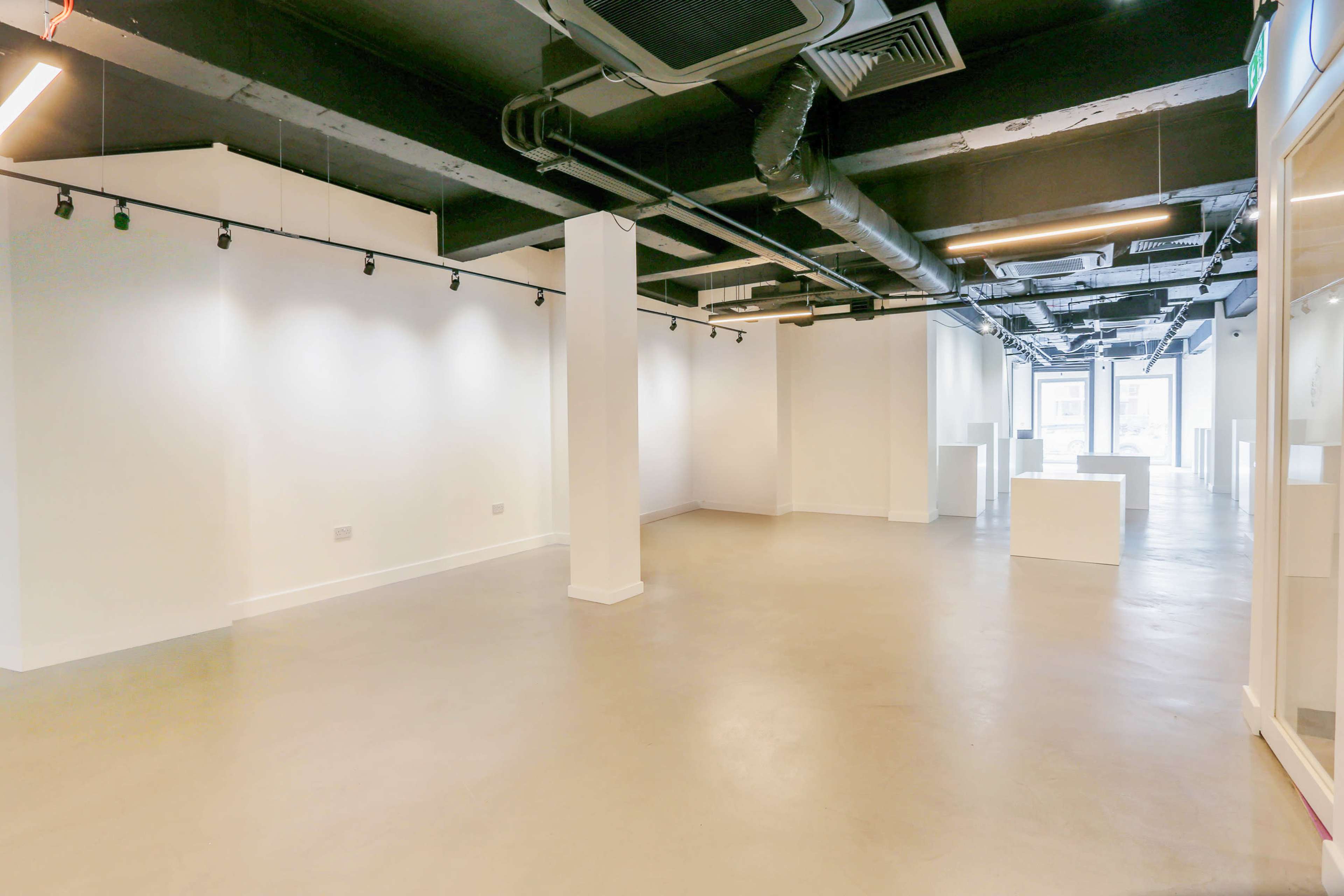 The image shows a spacious, empty commercial interior with white walls, concrete flooring, and exposed ceiling fixtures.