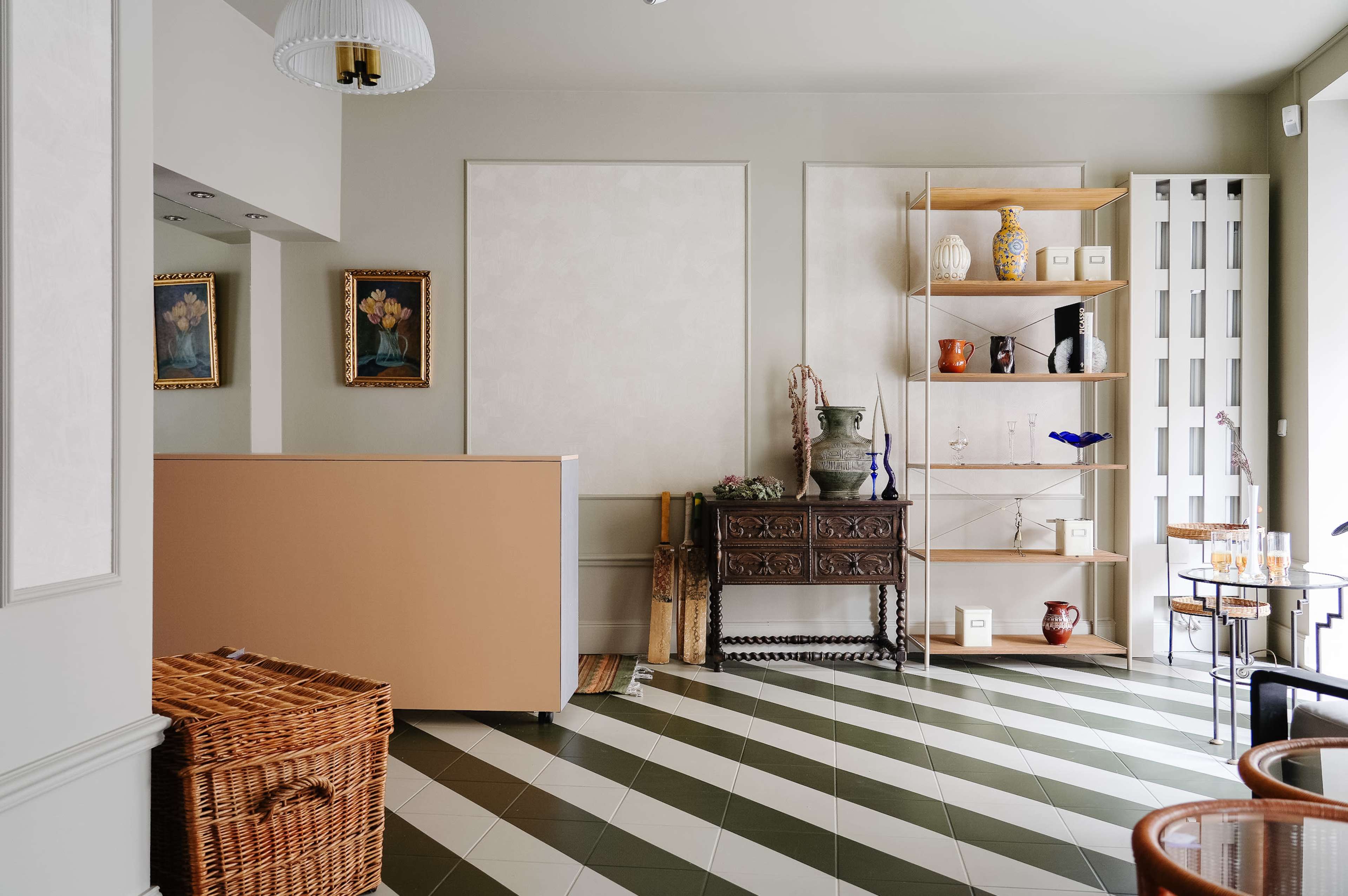 The image depicts a stylish interior of a room featuring a reception counter, decorative shelving unit, and a woven basket on the floor.