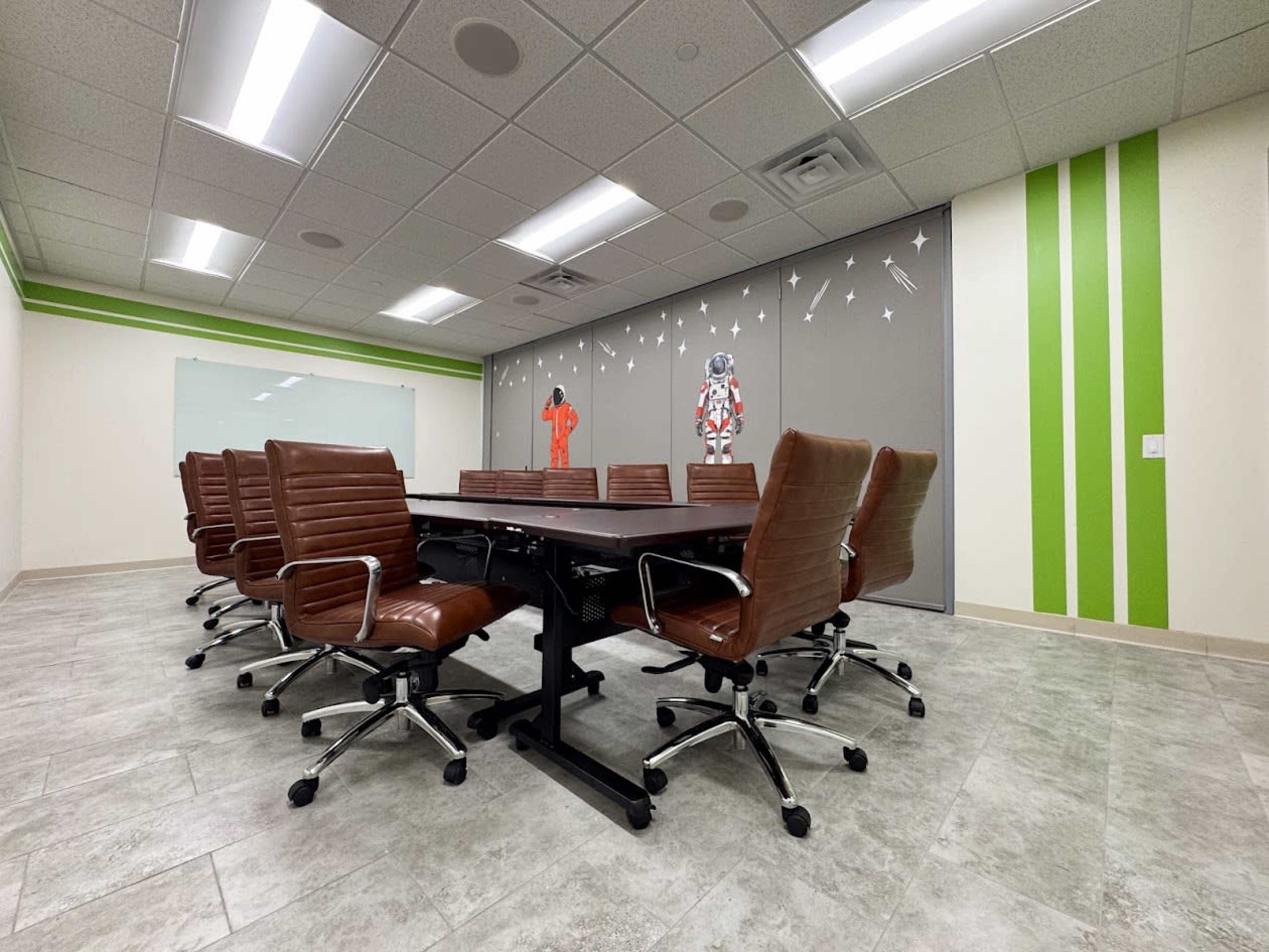 A modern conference room features a large table surrounded by brown leather chairs and a wall decorated with space-themed artwork.