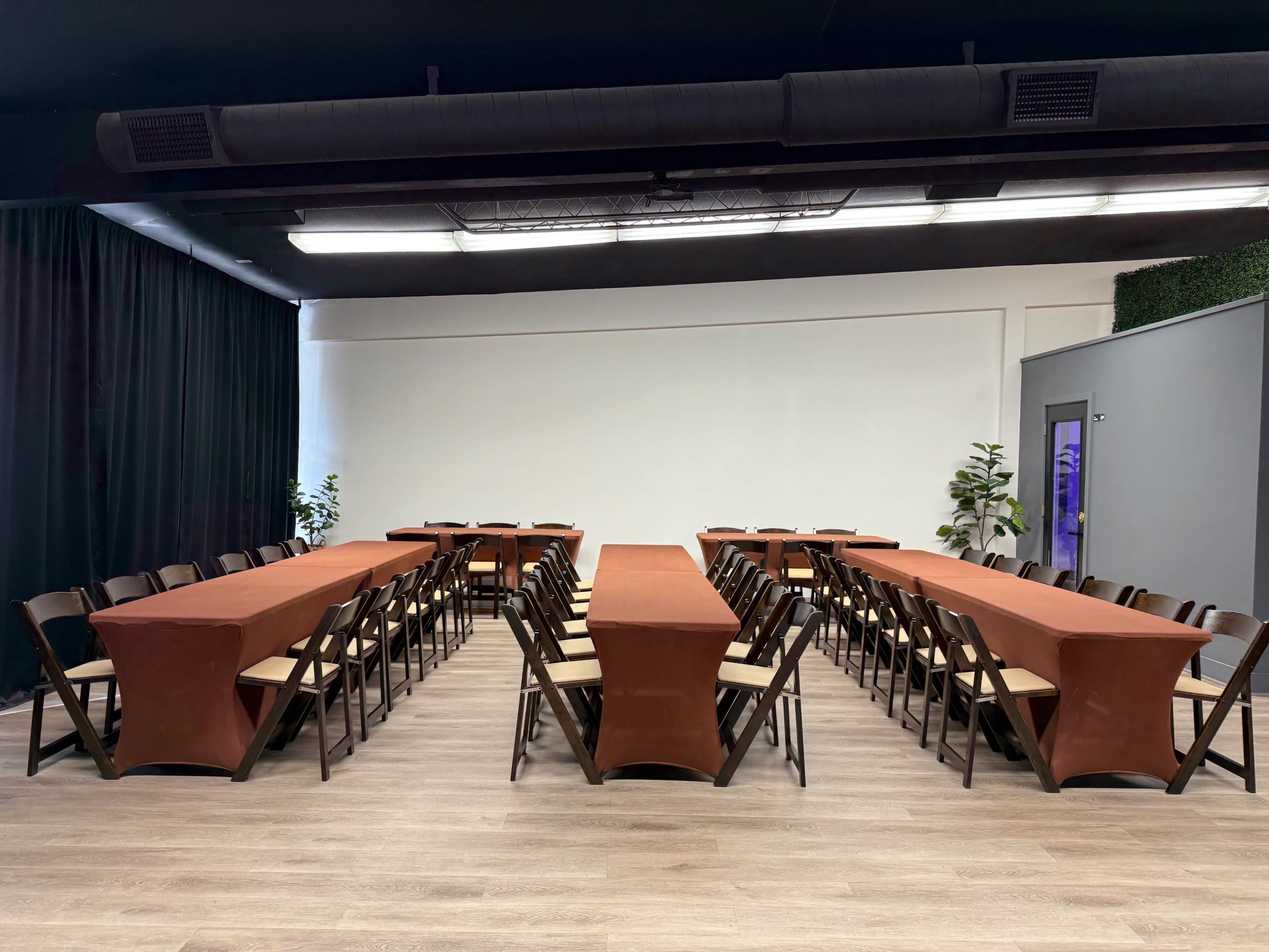 The image shows a spacious meeting room with two rows of long tables covered in orange tablecloths, arranged in a U-shape, with black chairs around them.