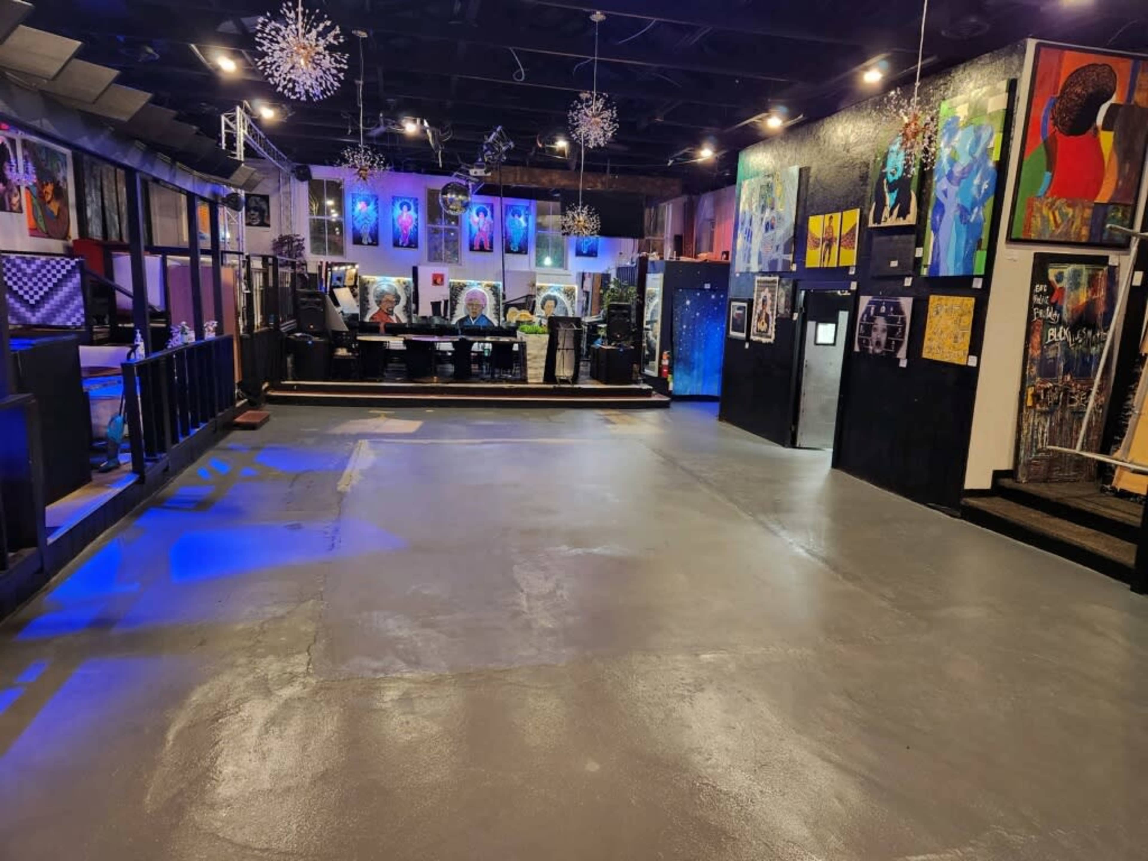 An empty art gallery or event space with various artworks displayed on the walls and a bar area in the background.