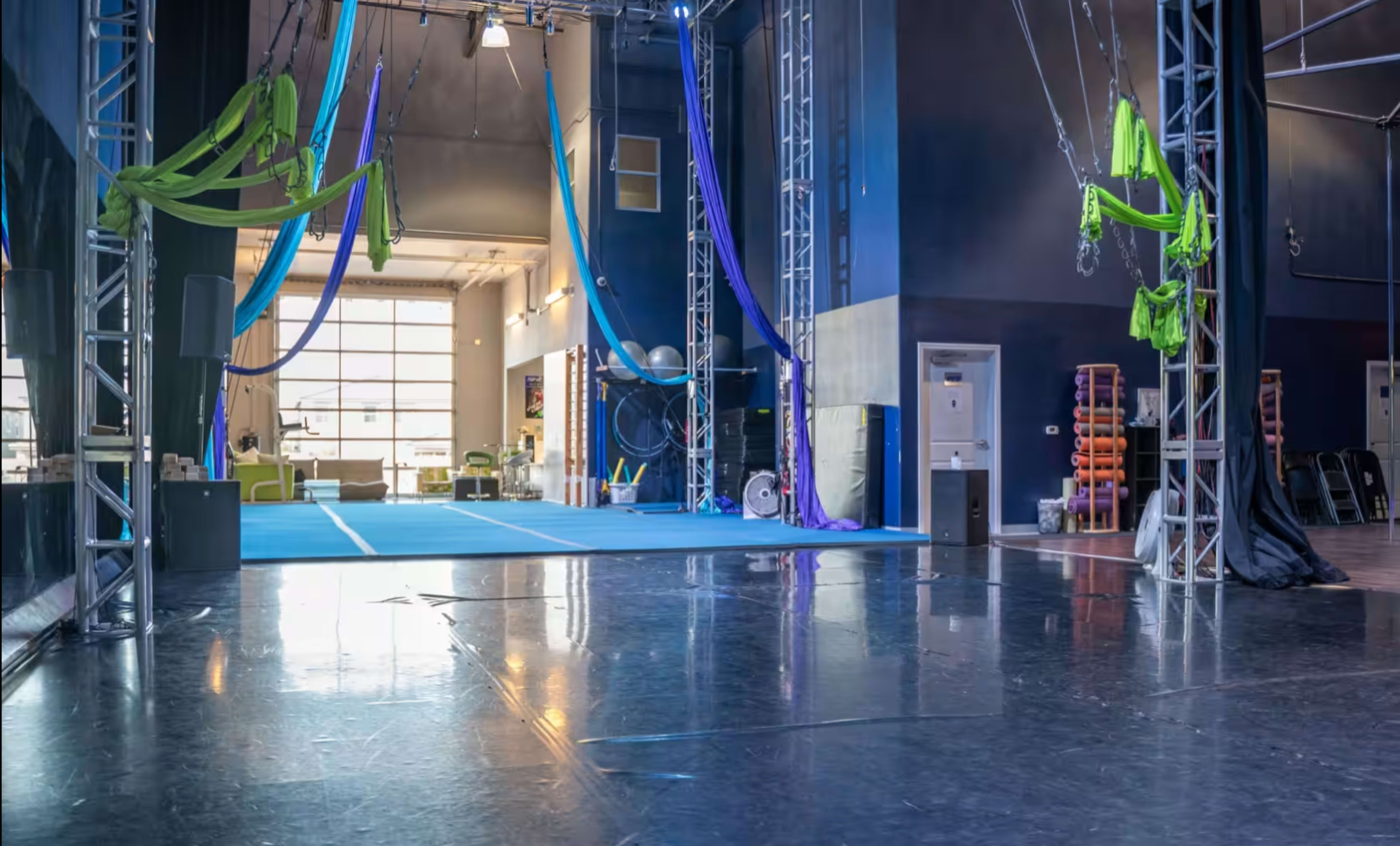 A spacious aerial silk studio with colorful silks hanging from the ceiling and a polished floor reflecting the lighting.