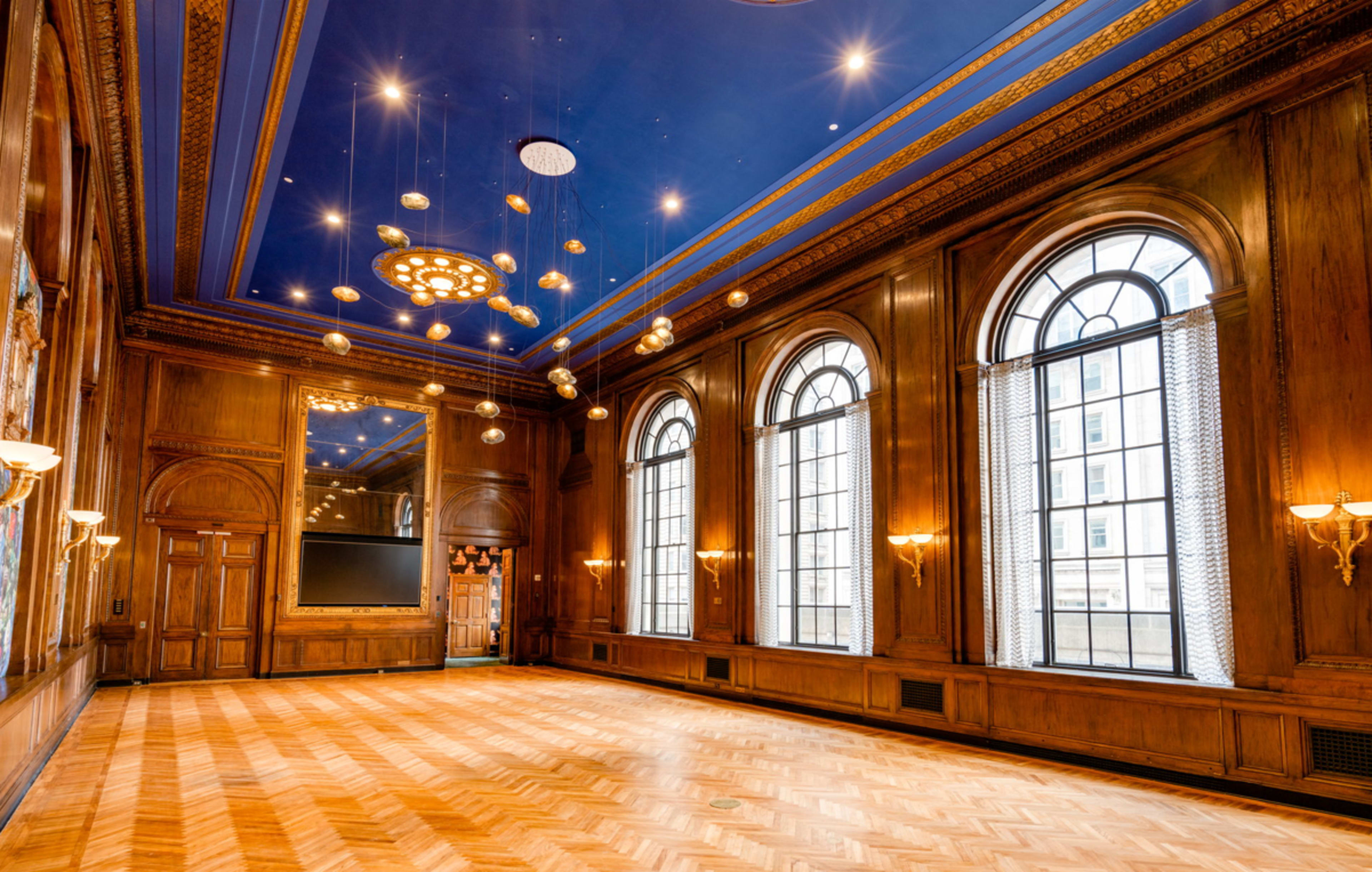 A spacious room with wooden walls, large arched windows, a blue ceiling, and decorative lighting fixtures.