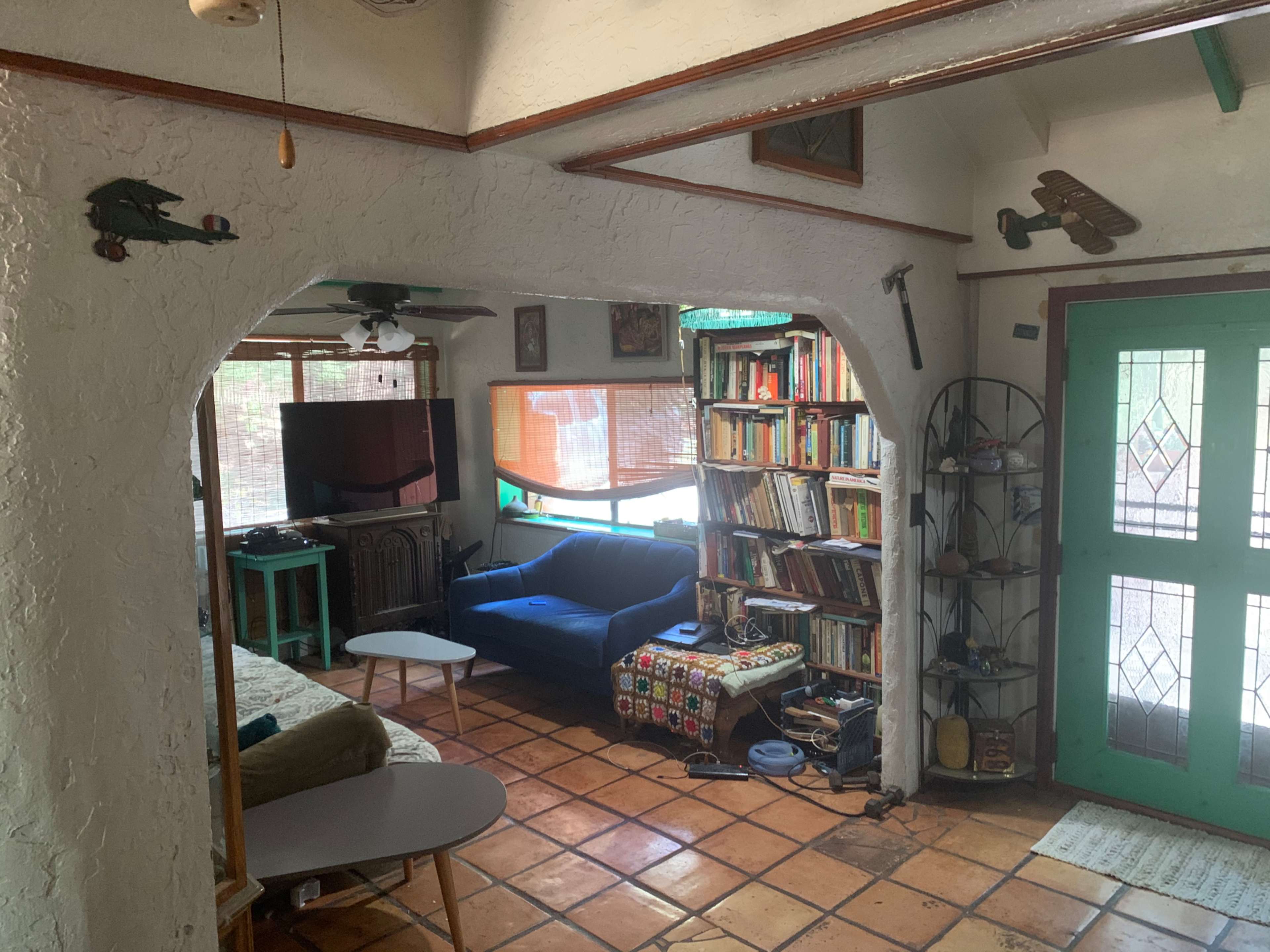 A living room features a blue couch, a bookshelf filled with books, and an arched entrance leading to a door with decorative glass panes.